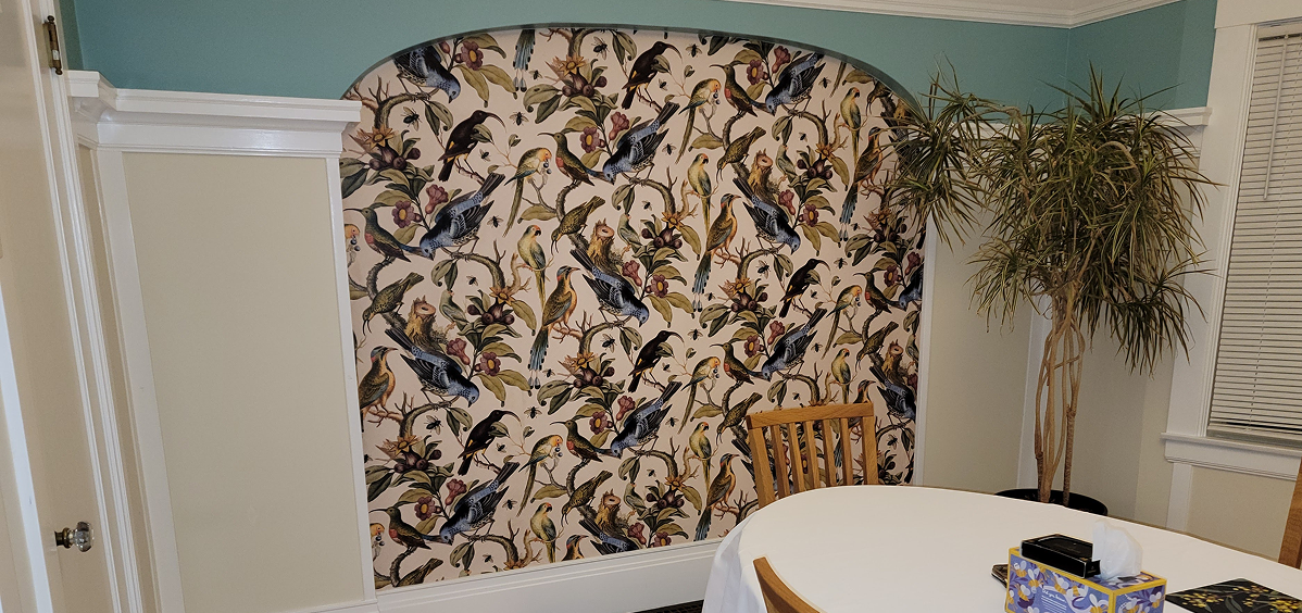 A wall with floral and bird wallpaper next to a wooden chair and table.