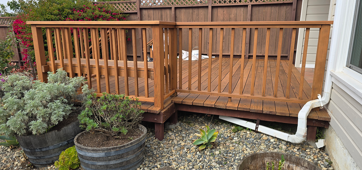 Wooden deck railing with a gate overlooking a garden bed.