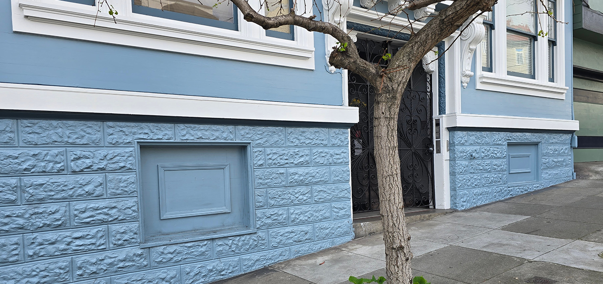 A blue-painted brick building with a leafless tree nearby.