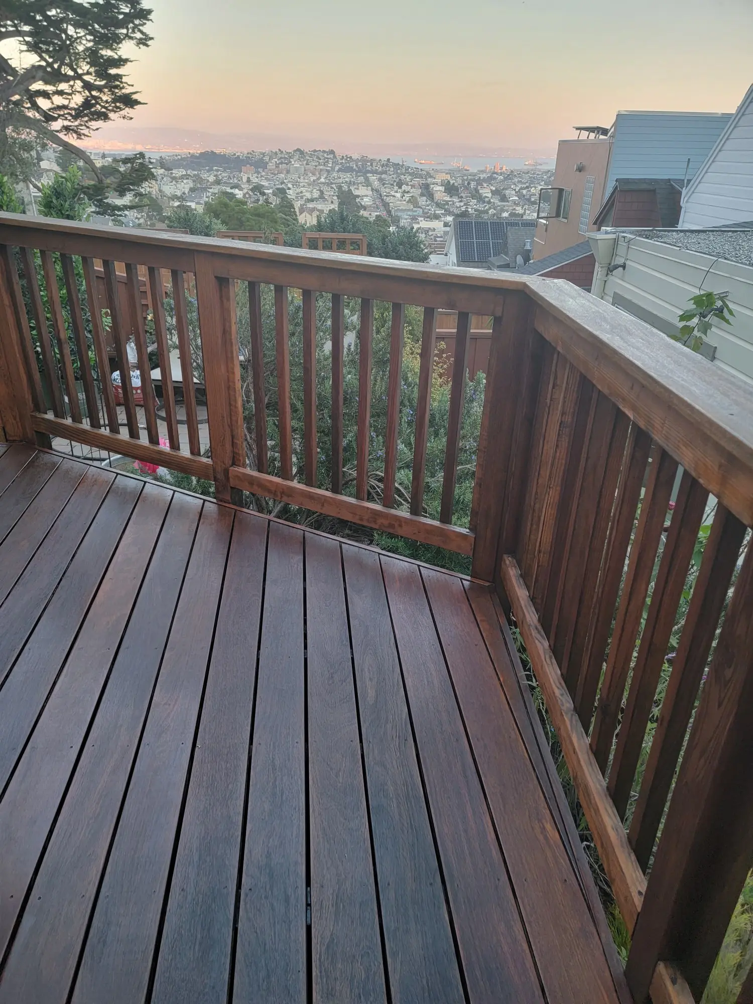 Wooden balcony with a scenic view of hills and houses.