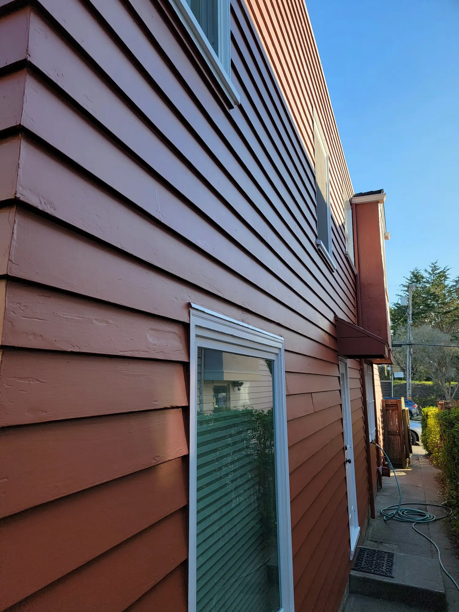 Close-up of a reddish-brown siding on a house with a window and outdoor light fixture.