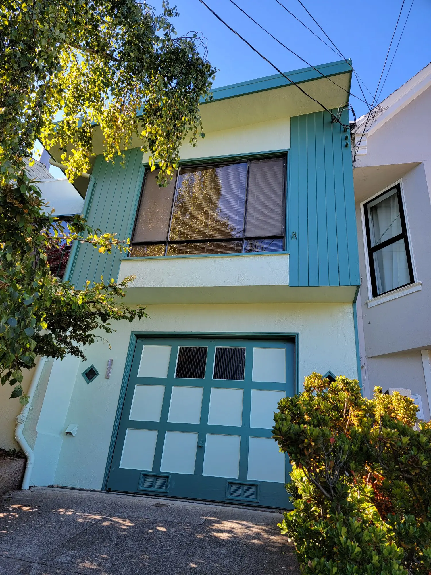 Two-story house with a garage and green trim surrounded by trees.
