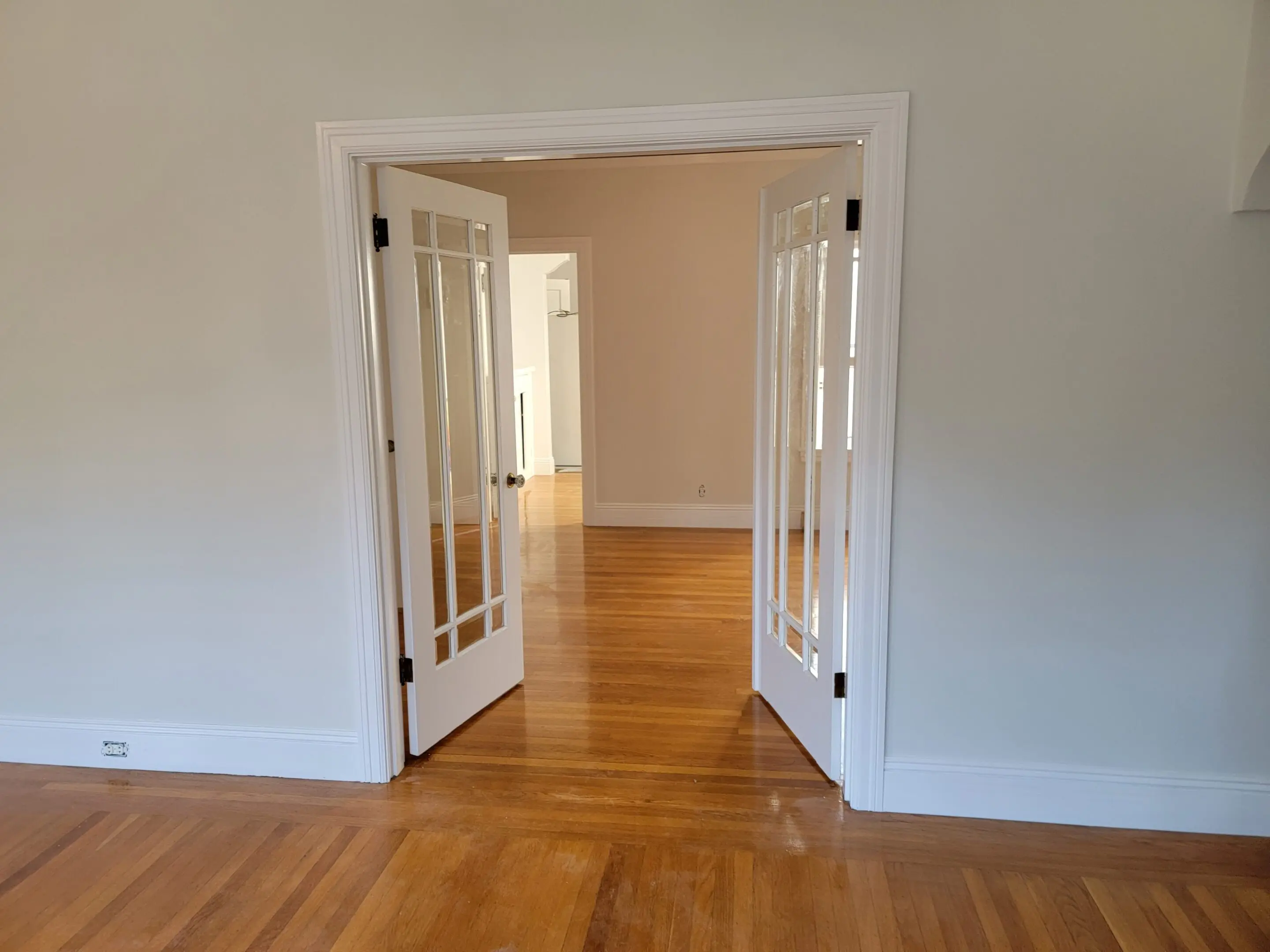 Open double doors leading to a bright, empty room with wooden floors.