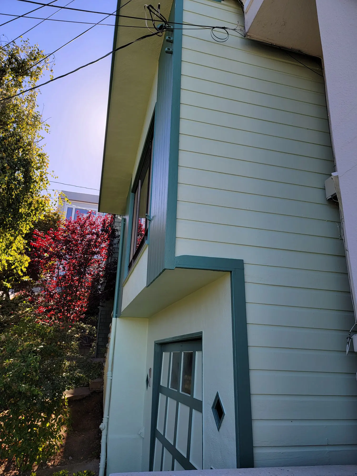 Side view of a light blue house with teal trim and surrounding trees.
