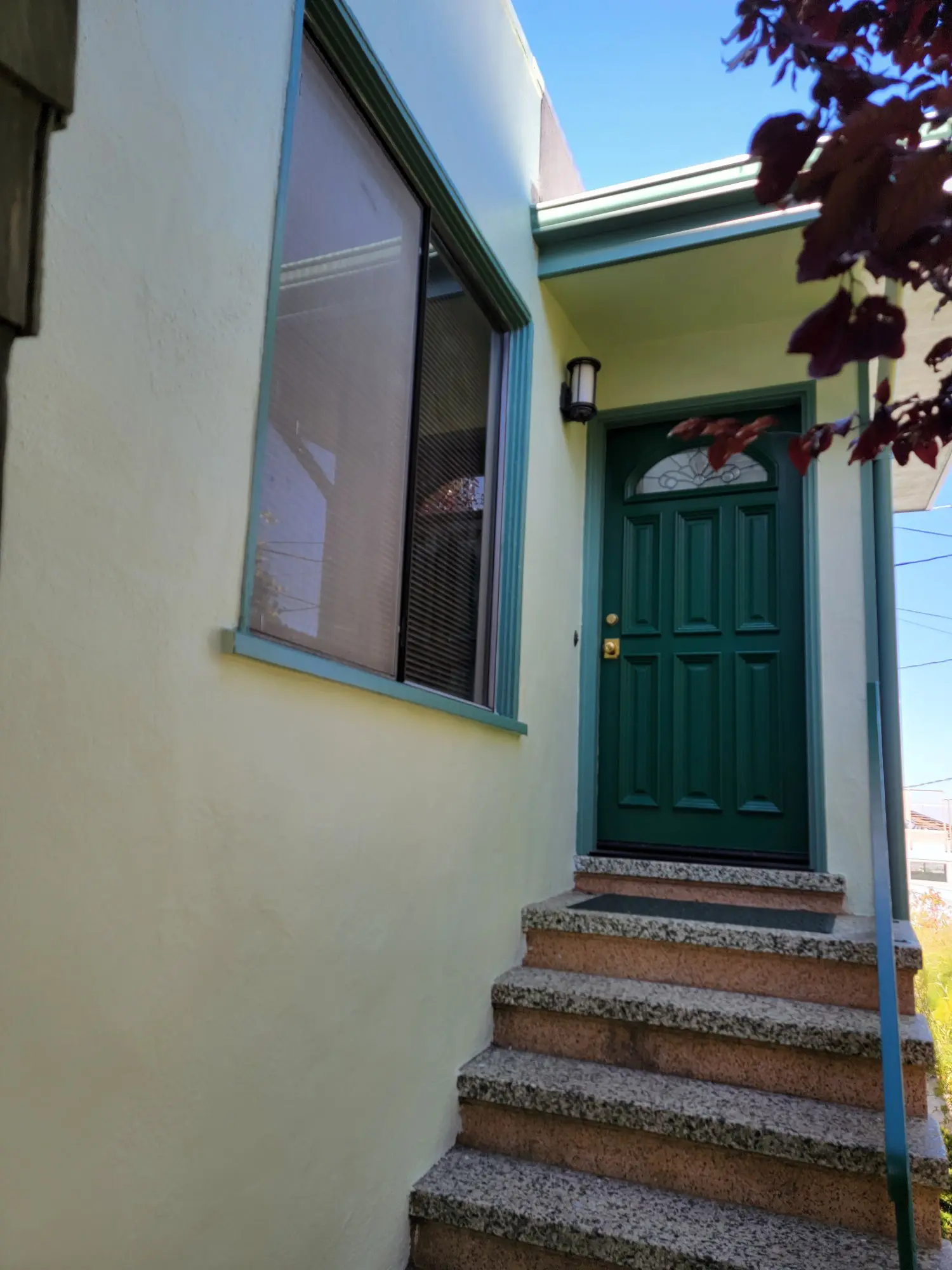 Green door with steps leading up to it on a yellow house exterior.