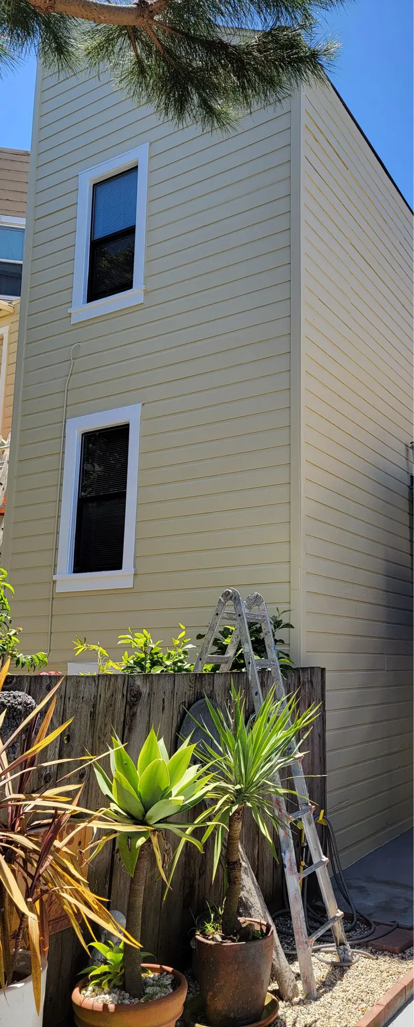 A beige house exterior with a small window and a ladder leaning against it.