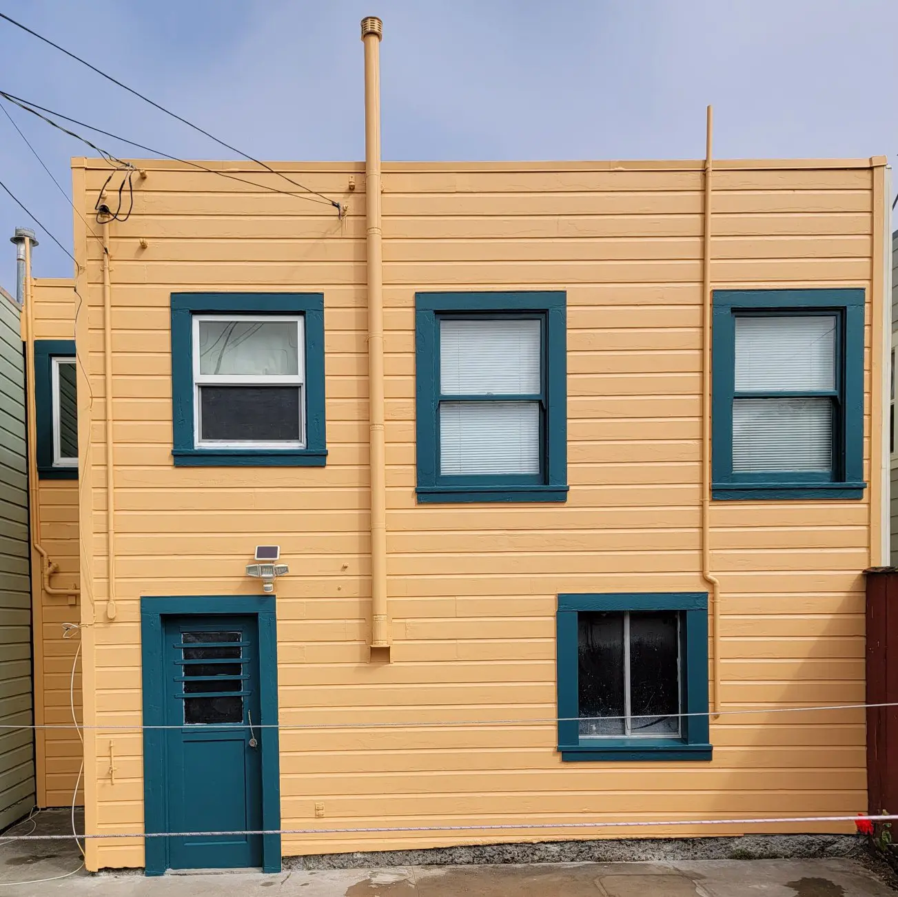 A yellow building facade with blue-trimmed windows and door under a clear sky.