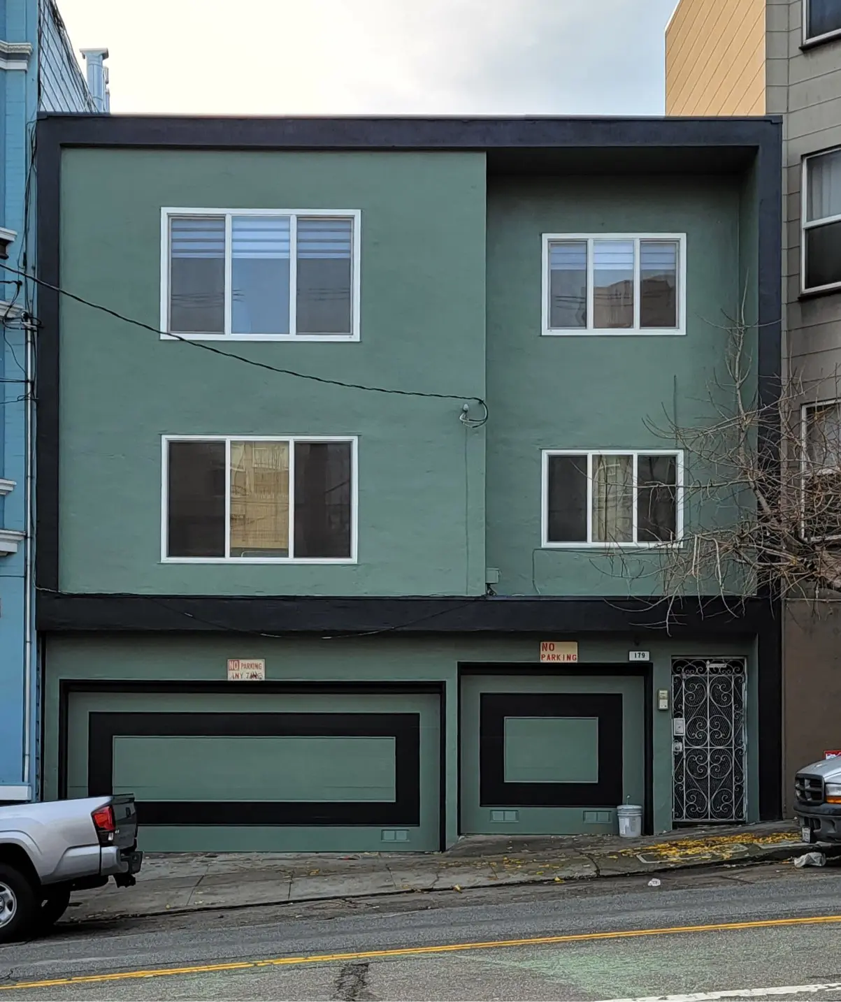 Green three-story residential building with two garage doors and windows.