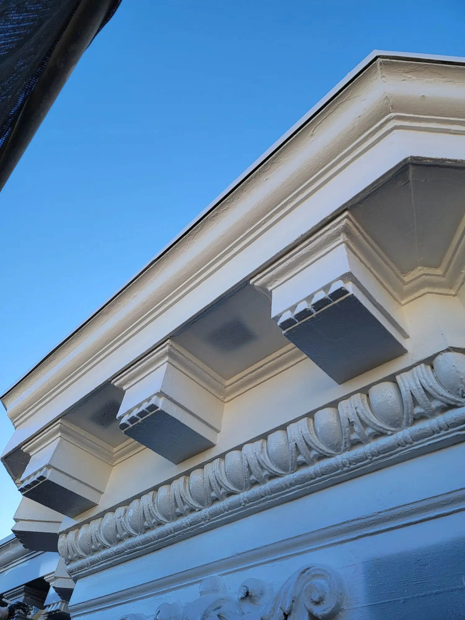 Ornate architectural details on a building's cornice against a clear blue sky.