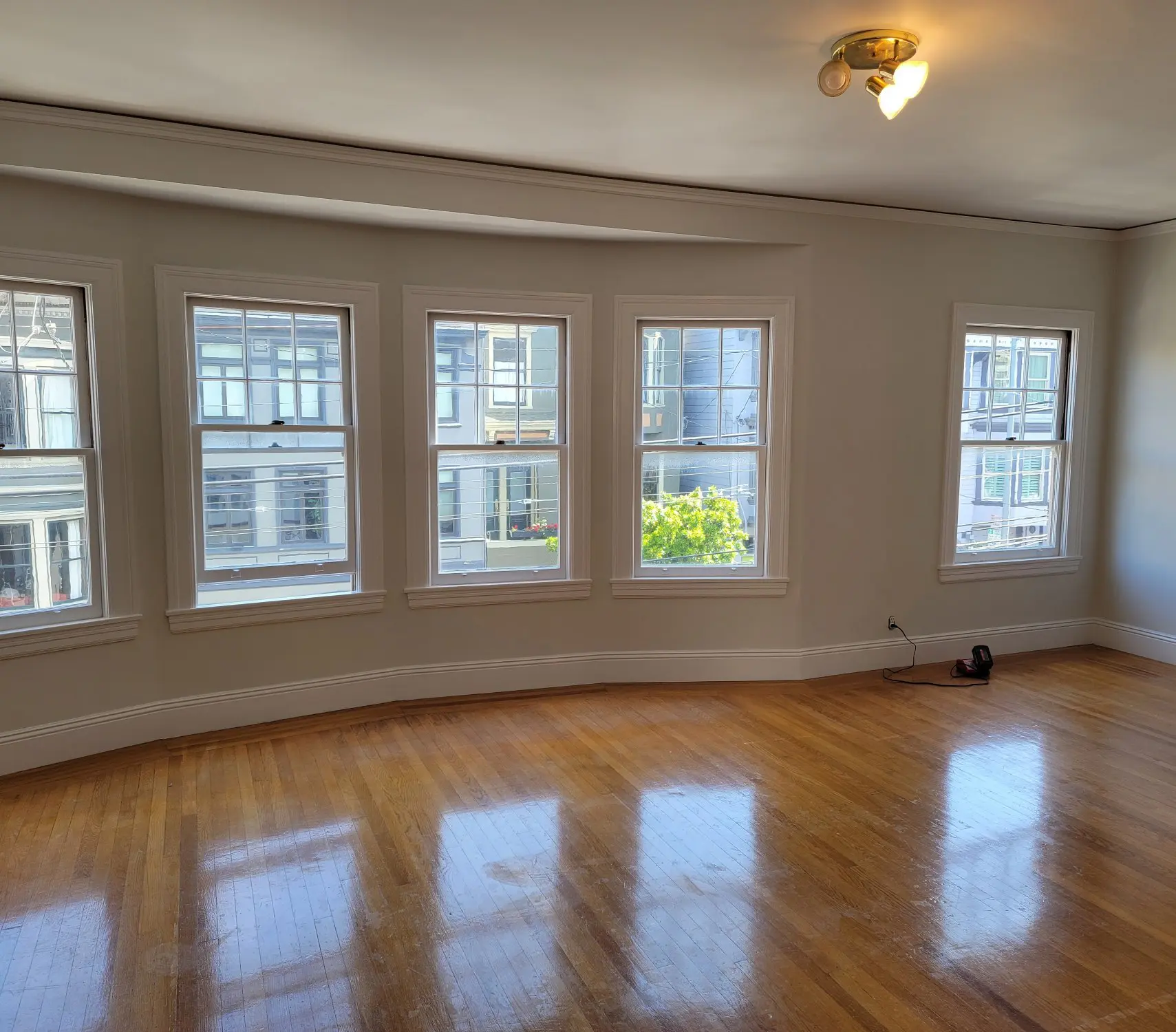 Empty room with large windows and polished wooden floor.