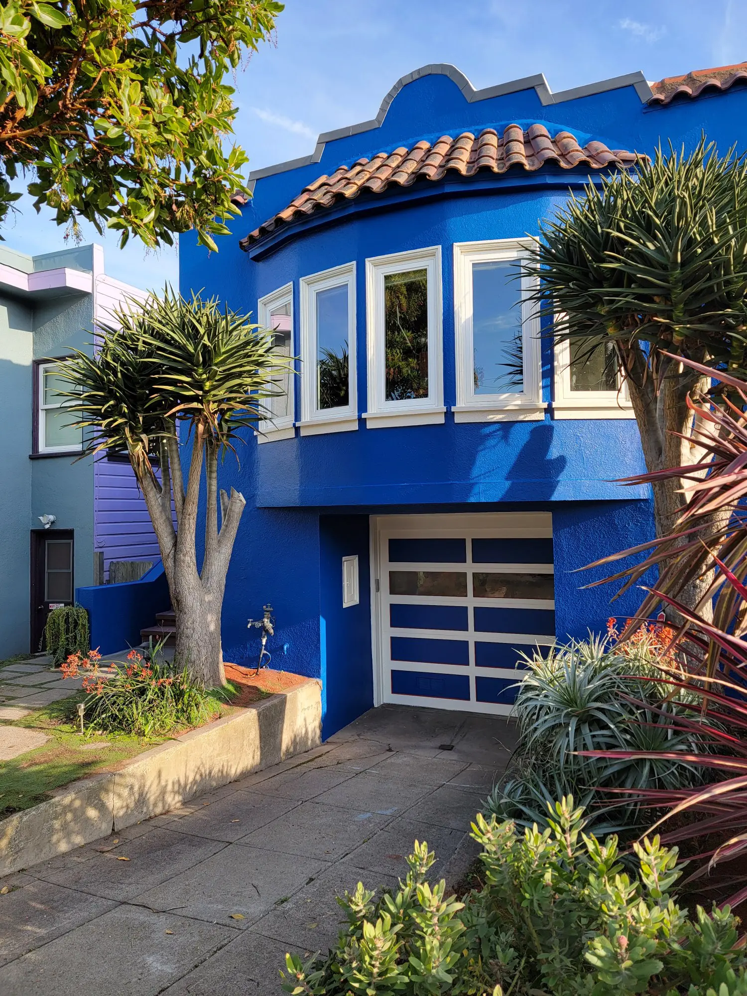 Bright blue house with unique rounded windows and lush greenery.
