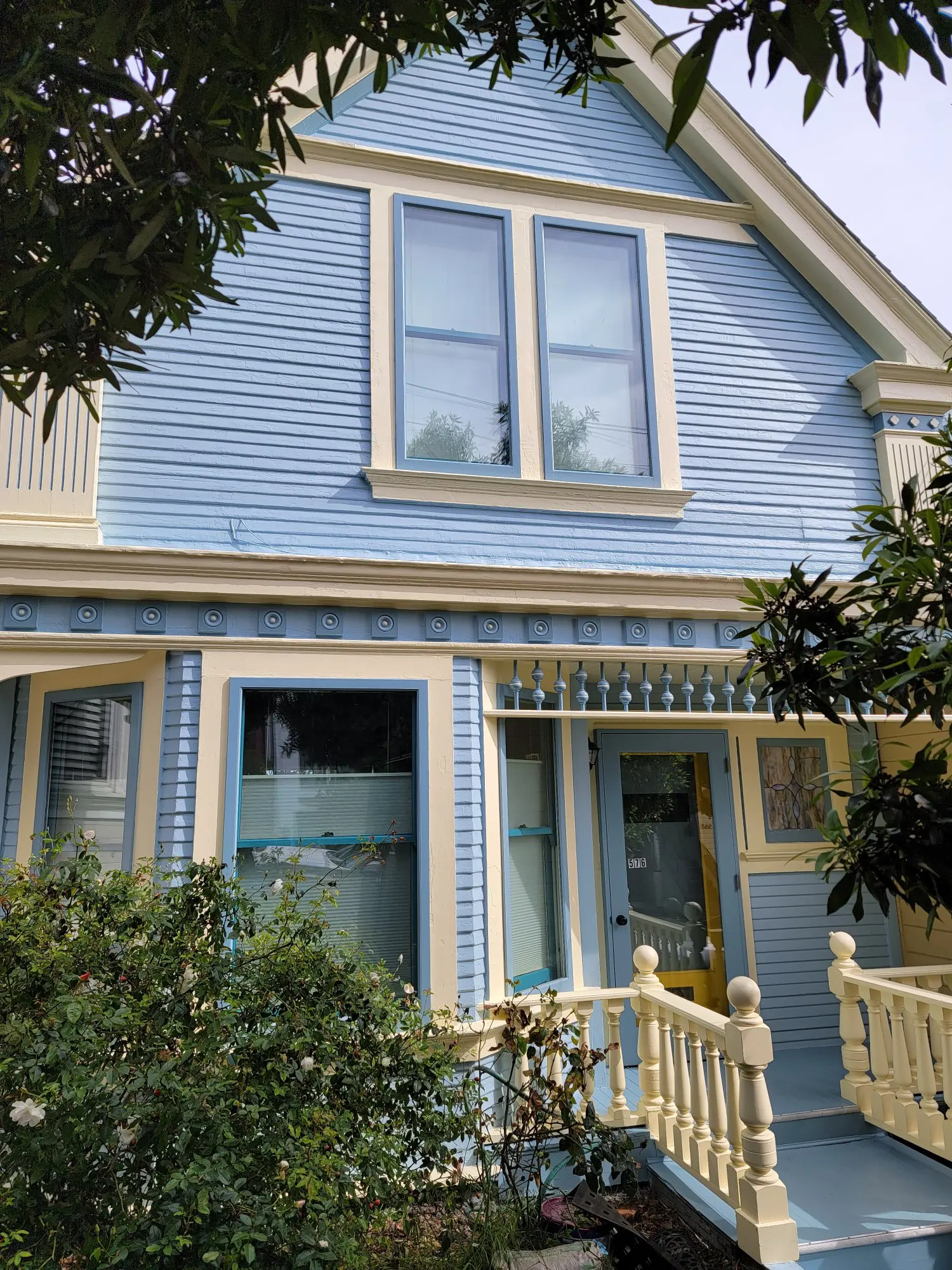 A charming blue Victorian house with white trim and large windows.