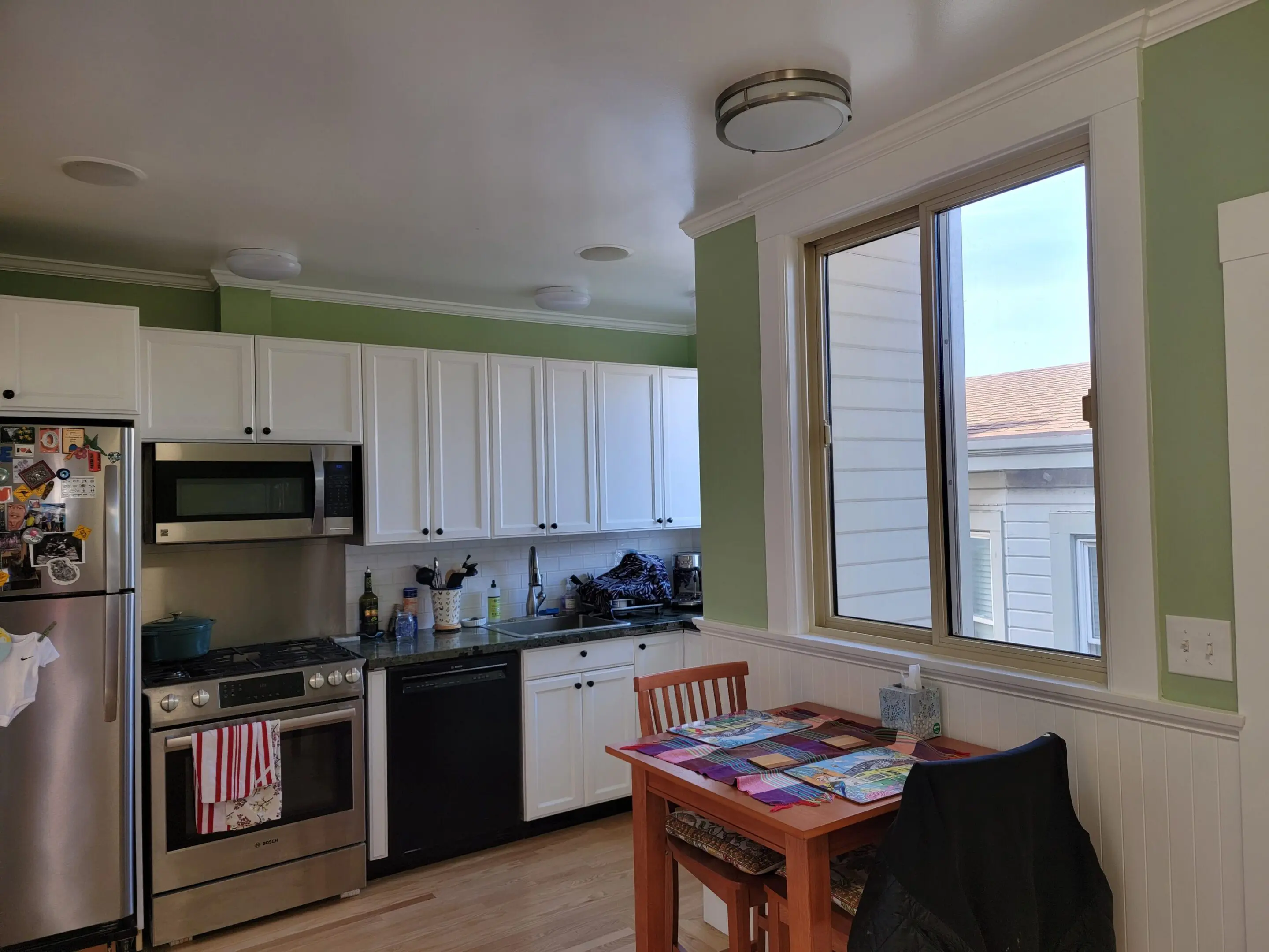 Bright kitchen with white cabinets and a cozy dining table near a large window.