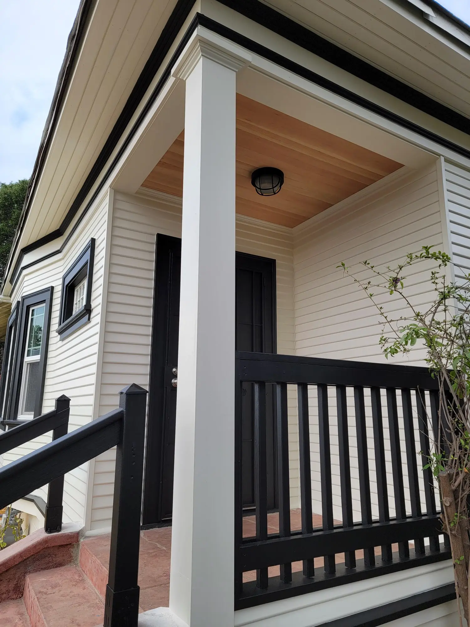 A cozy porch with black railing and white siding on a house.