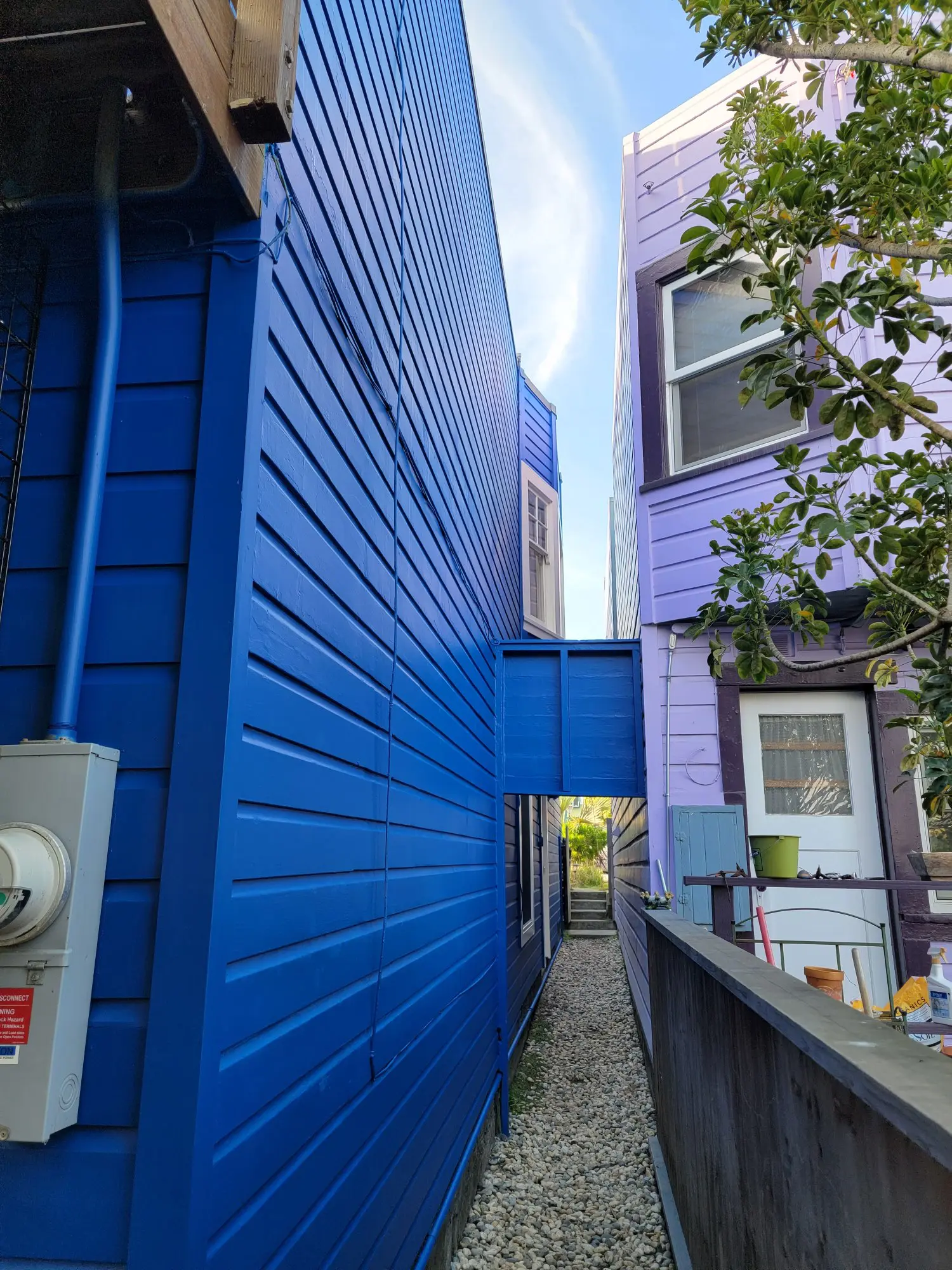 Narrow alley between vibrant blue buildings under a bright sky.