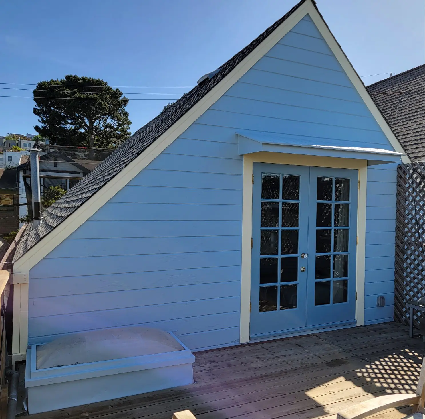 A light blue triangular house with French doors and a bench.