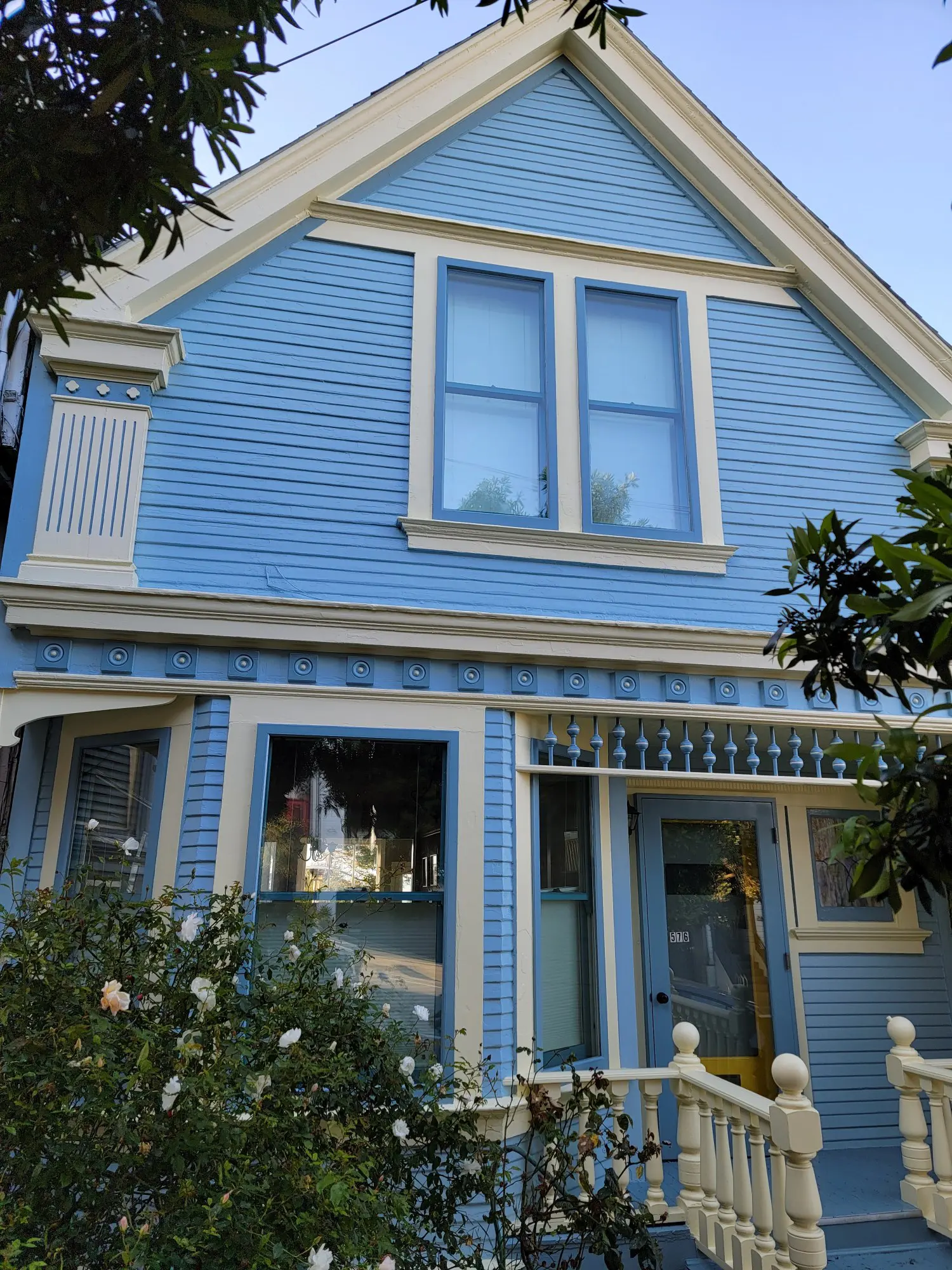A charming blue Victorian house with white trim and a striped awning.