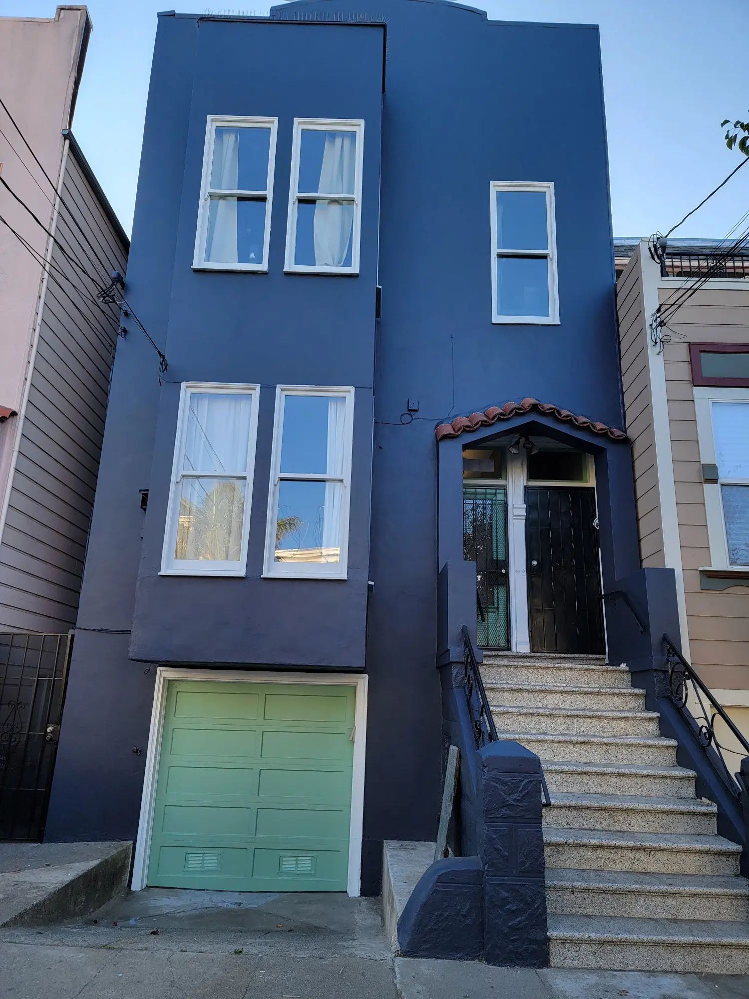 Blue townhouse with stairs and garage in an urban setting.