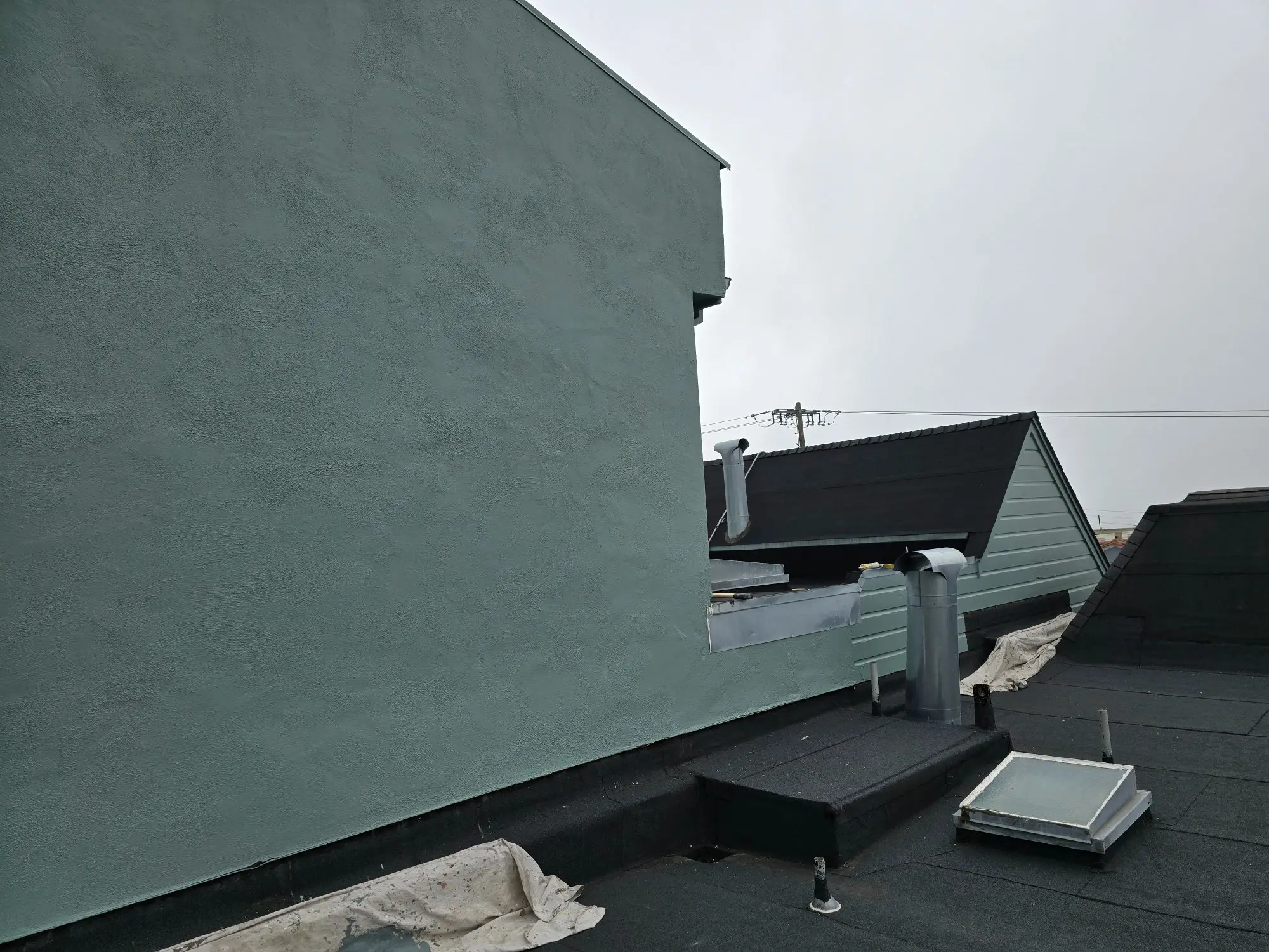 A gray wall with a black gutter system under a cloudy sky.