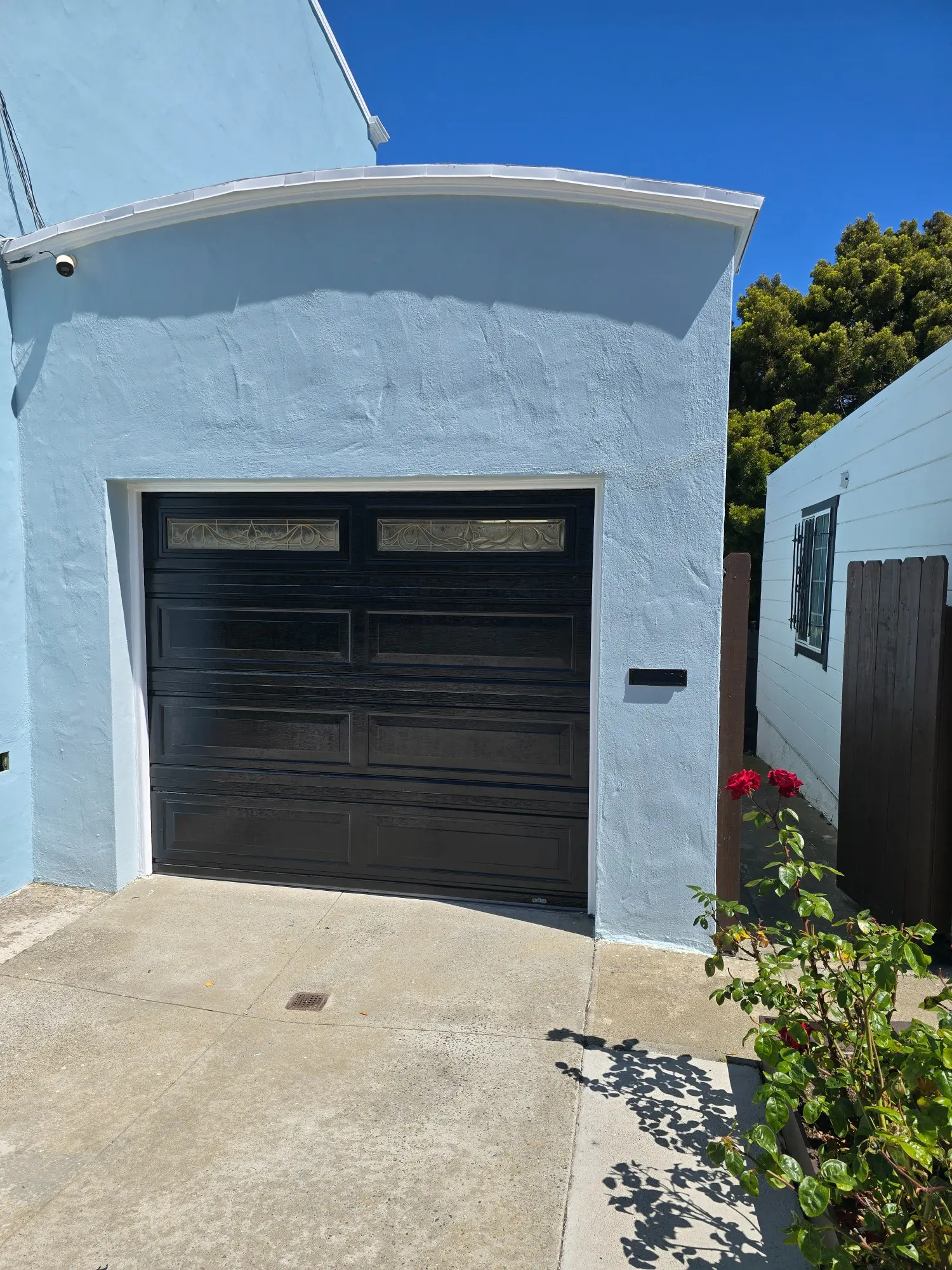 A black garage door set in a light blue house exterior under a clear sky.