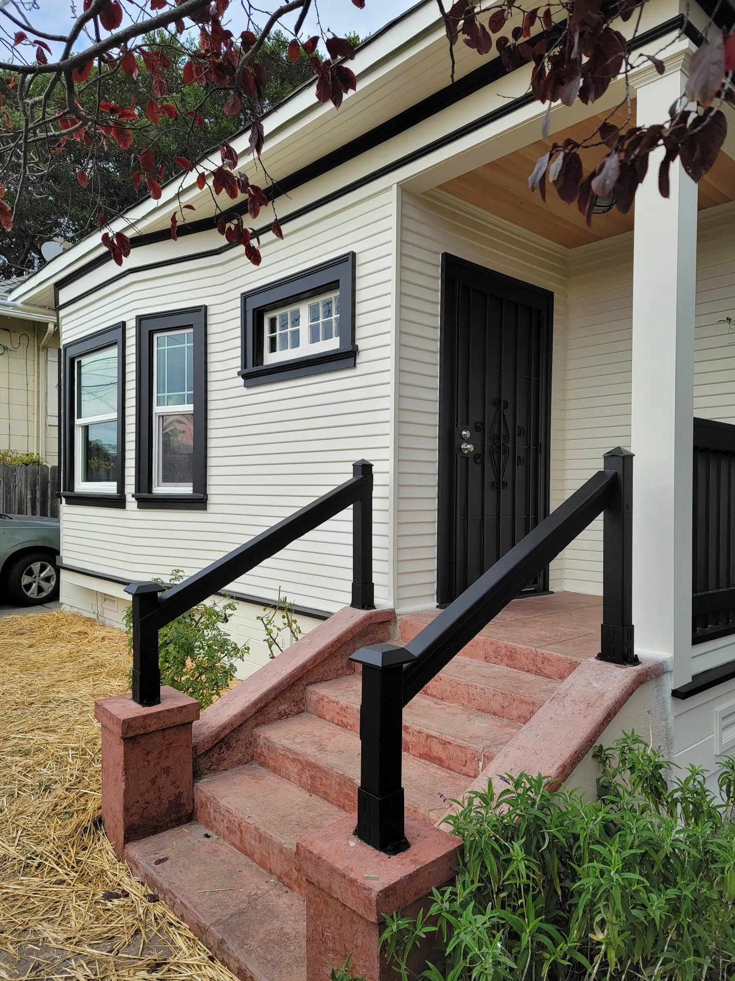 Small house entrance with red steps and black railings.