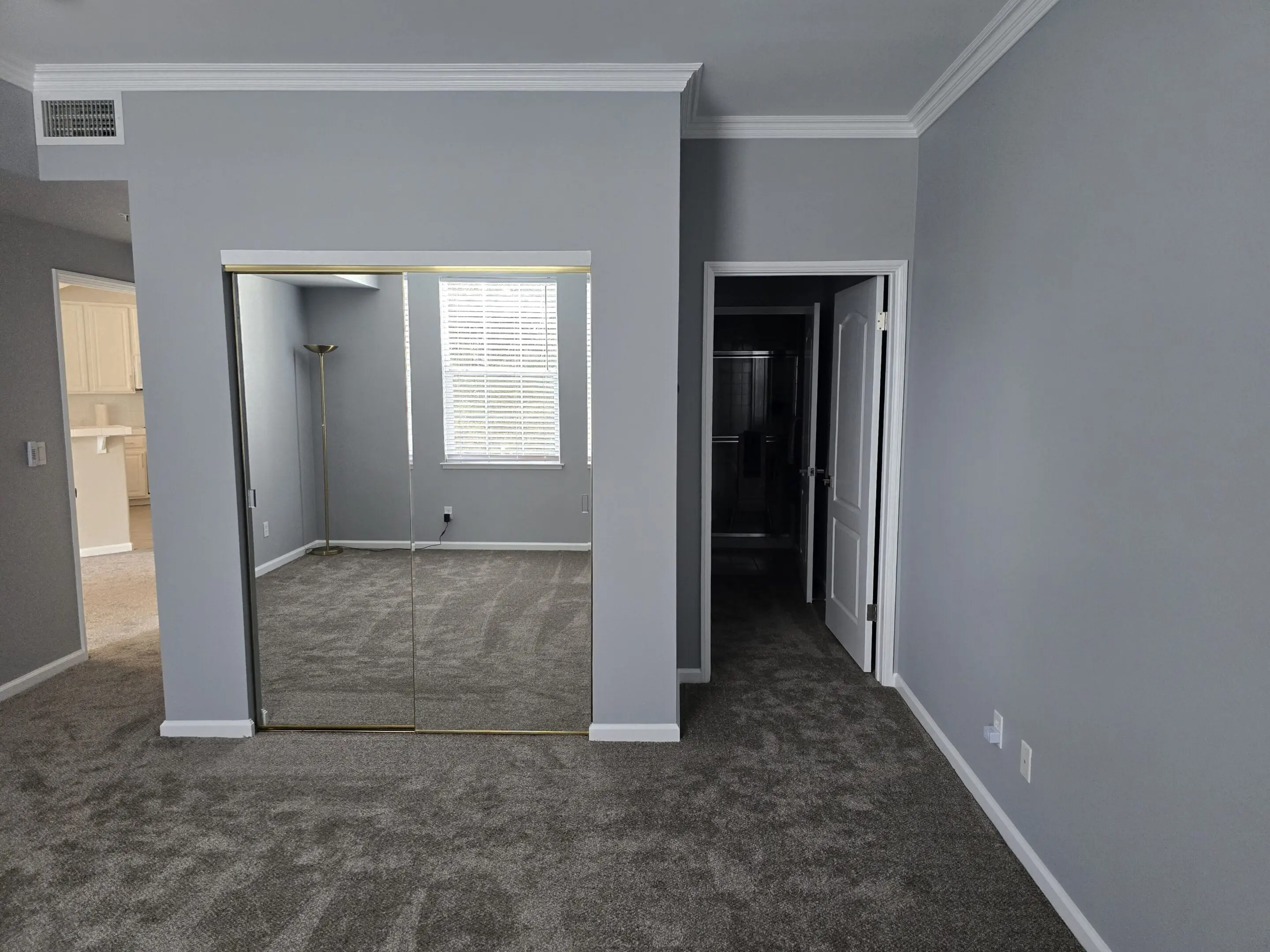 Empty room with gray walls and carpet, featuring a mirrored closet and doorways.