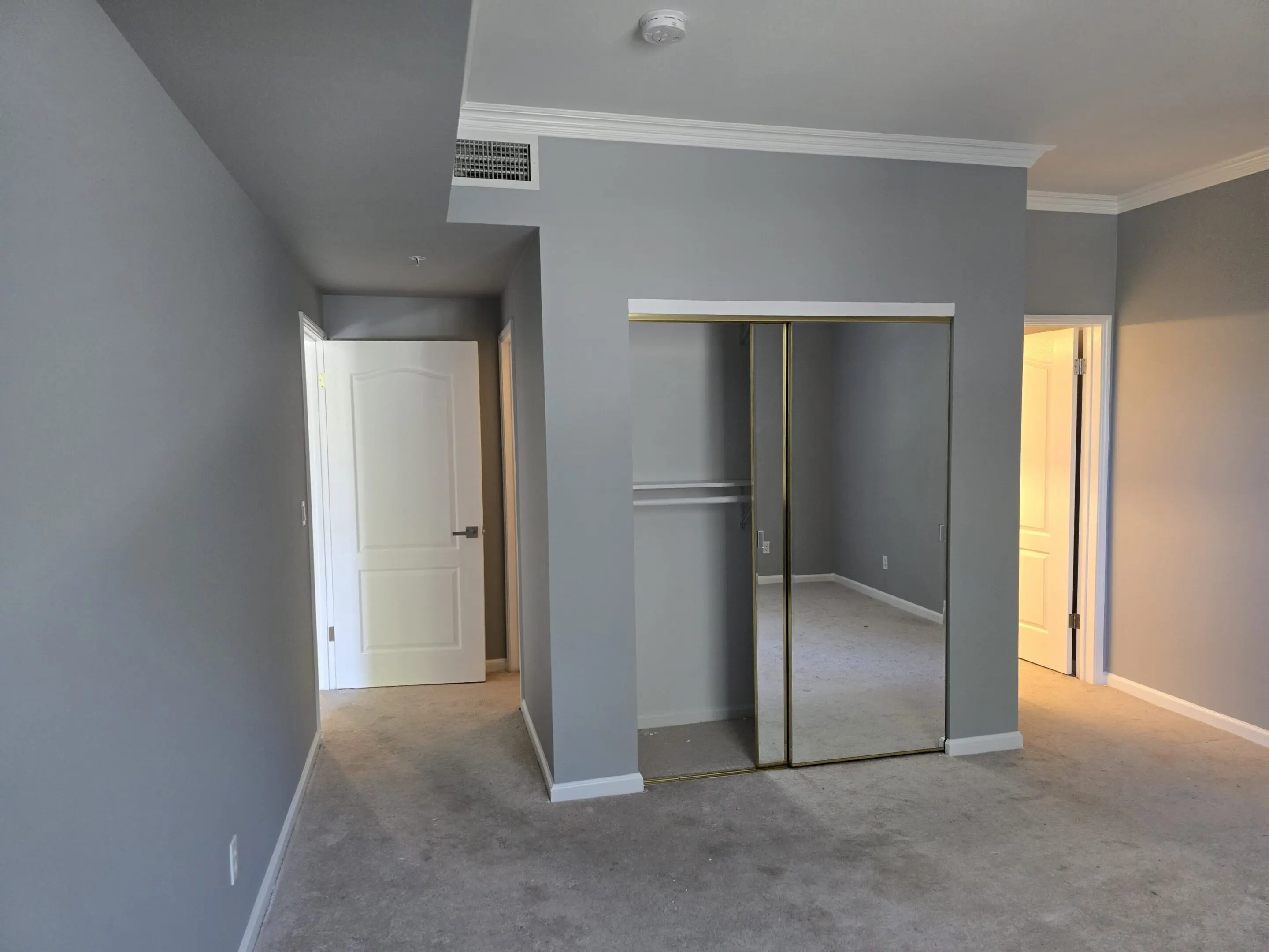 Empty bedroom with mirrored closet doors and neutral walls.