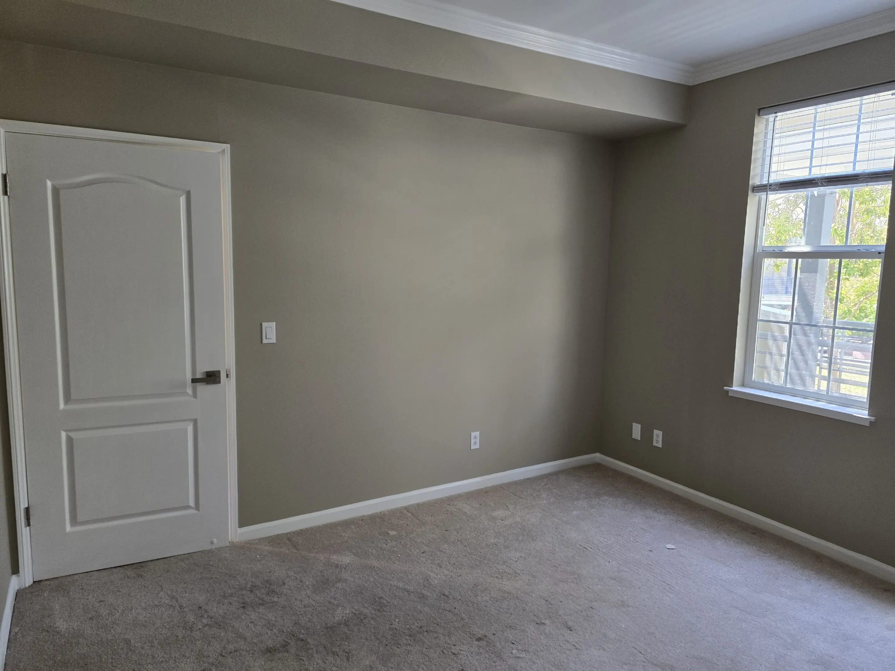 Empty bedroom with beige walls and carpeted floor.