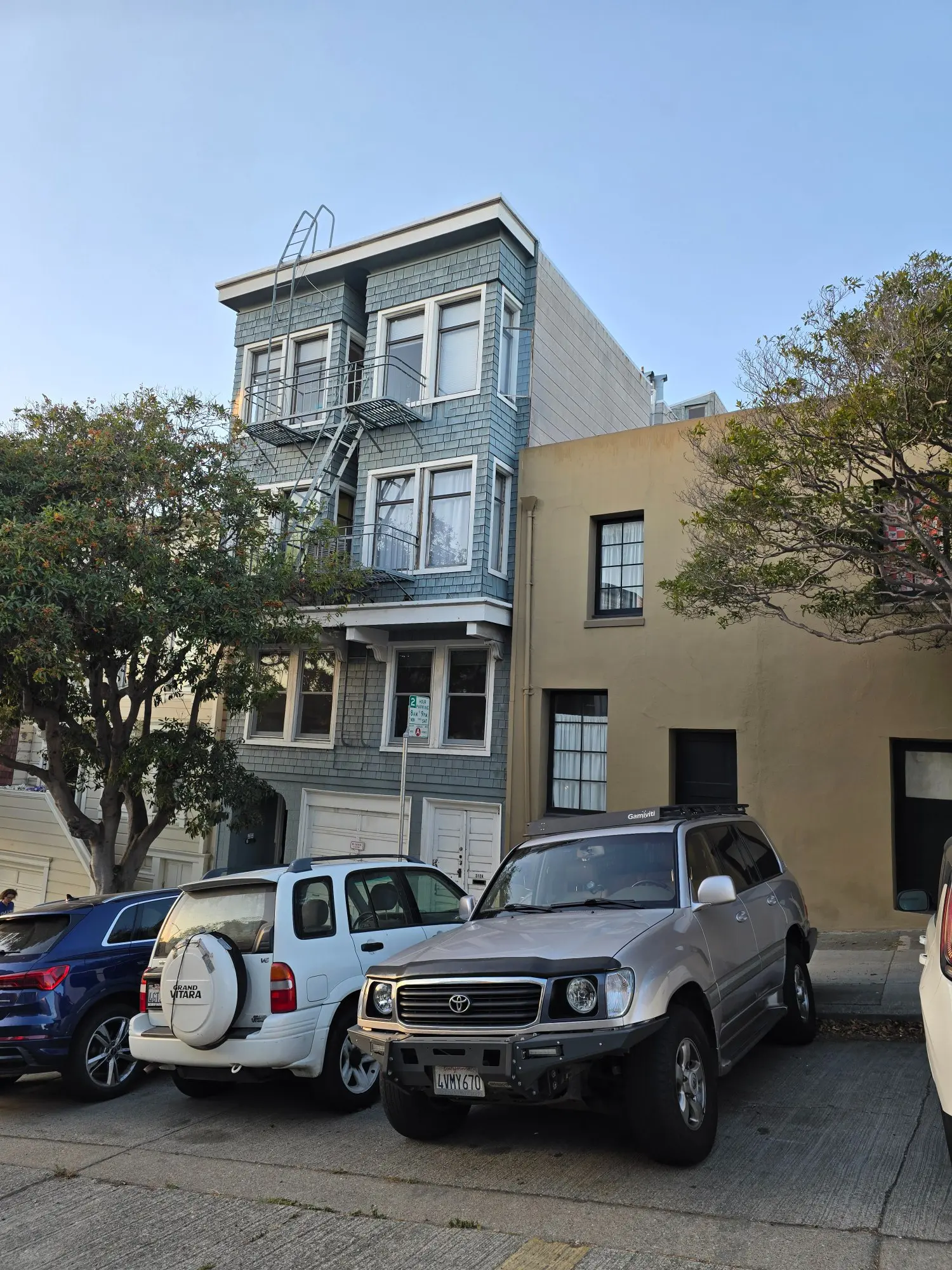 A street view of two adjacent buildings with parked cars in front.