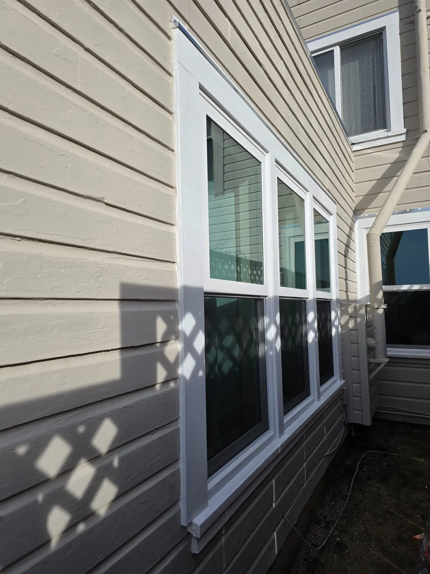 Sunlight casts geometric shadows on a beige house exterior with white-trimmed windows.