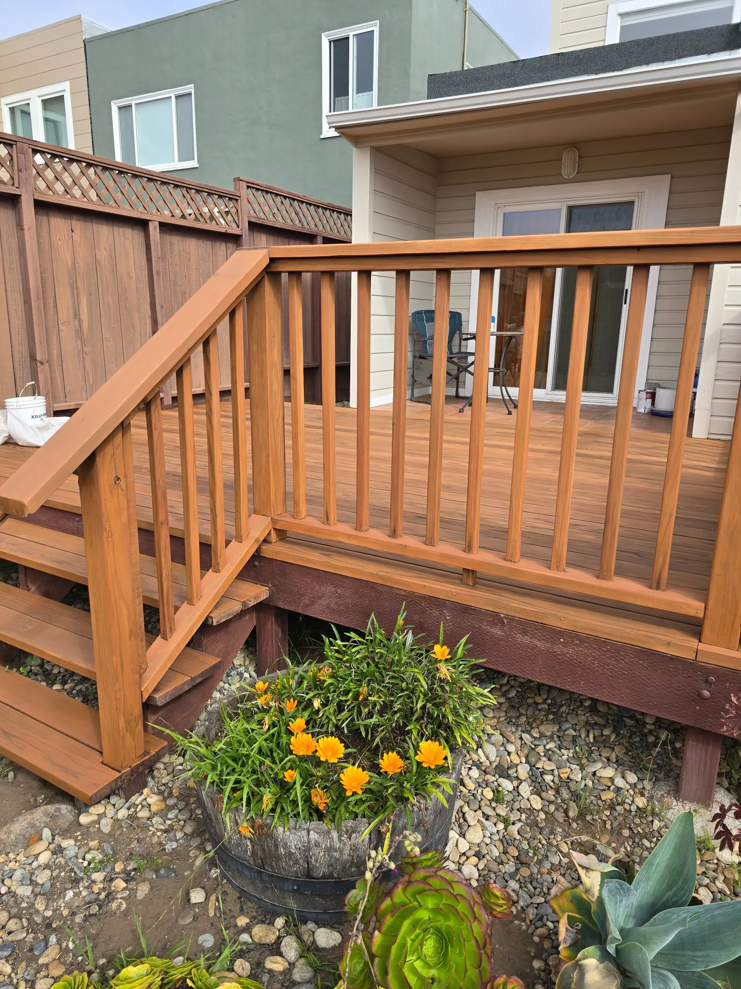 Wooden deck stairs leading to a patio with a flower bed below.