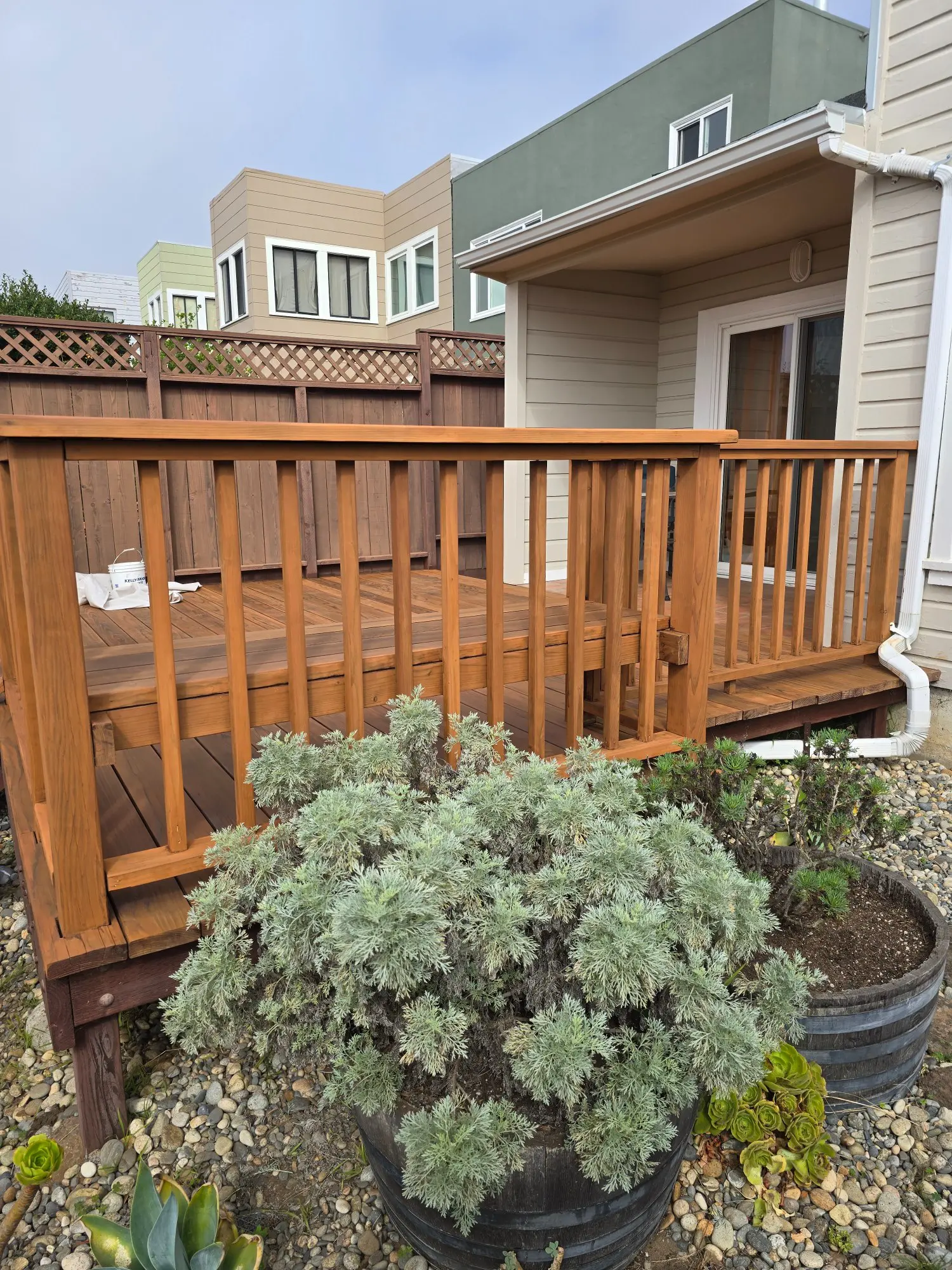 A wooden deck with railing attached to a house, surrounded by plants.