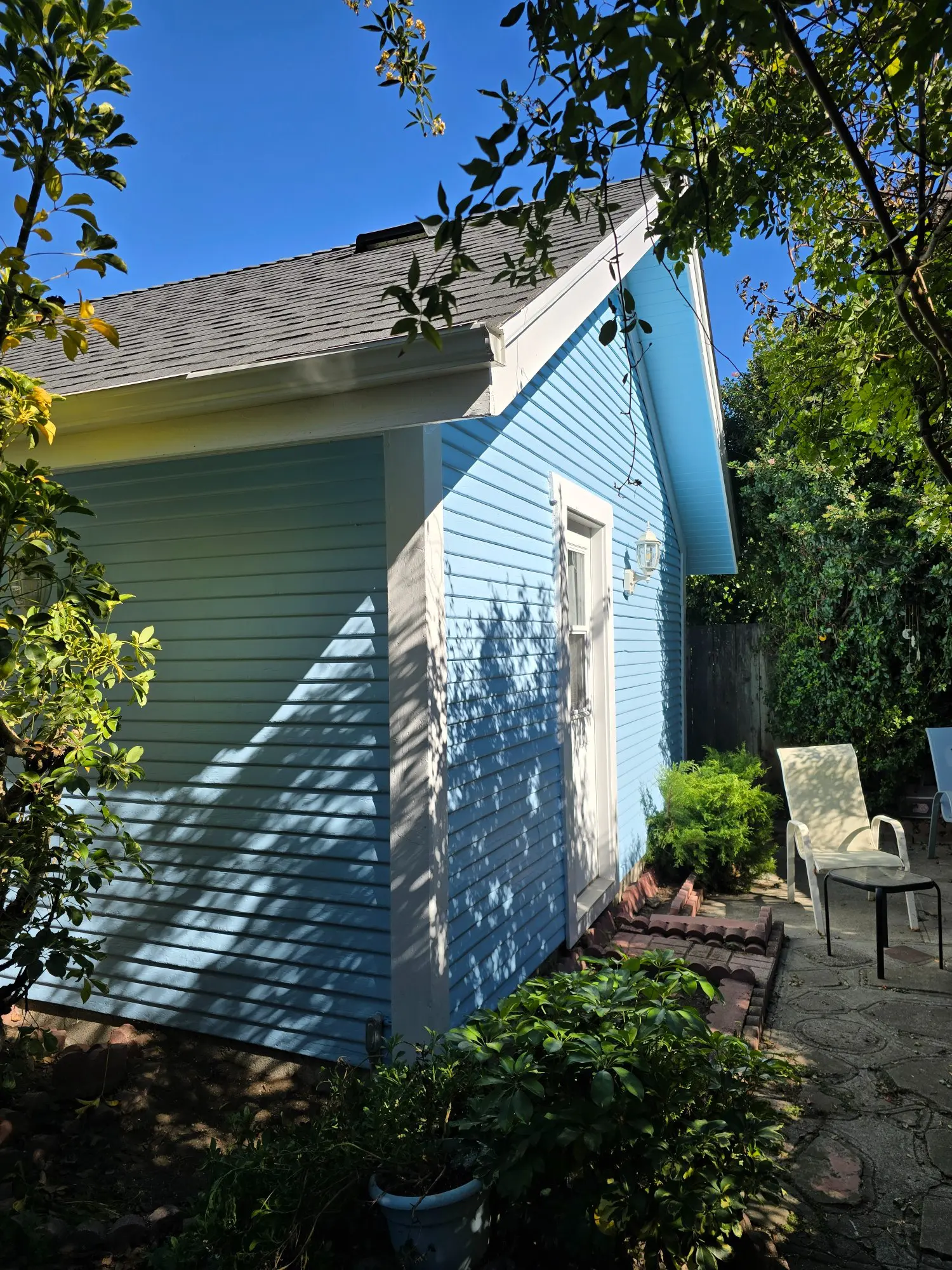 Blue-sided house with outdoor chairs and greenery.