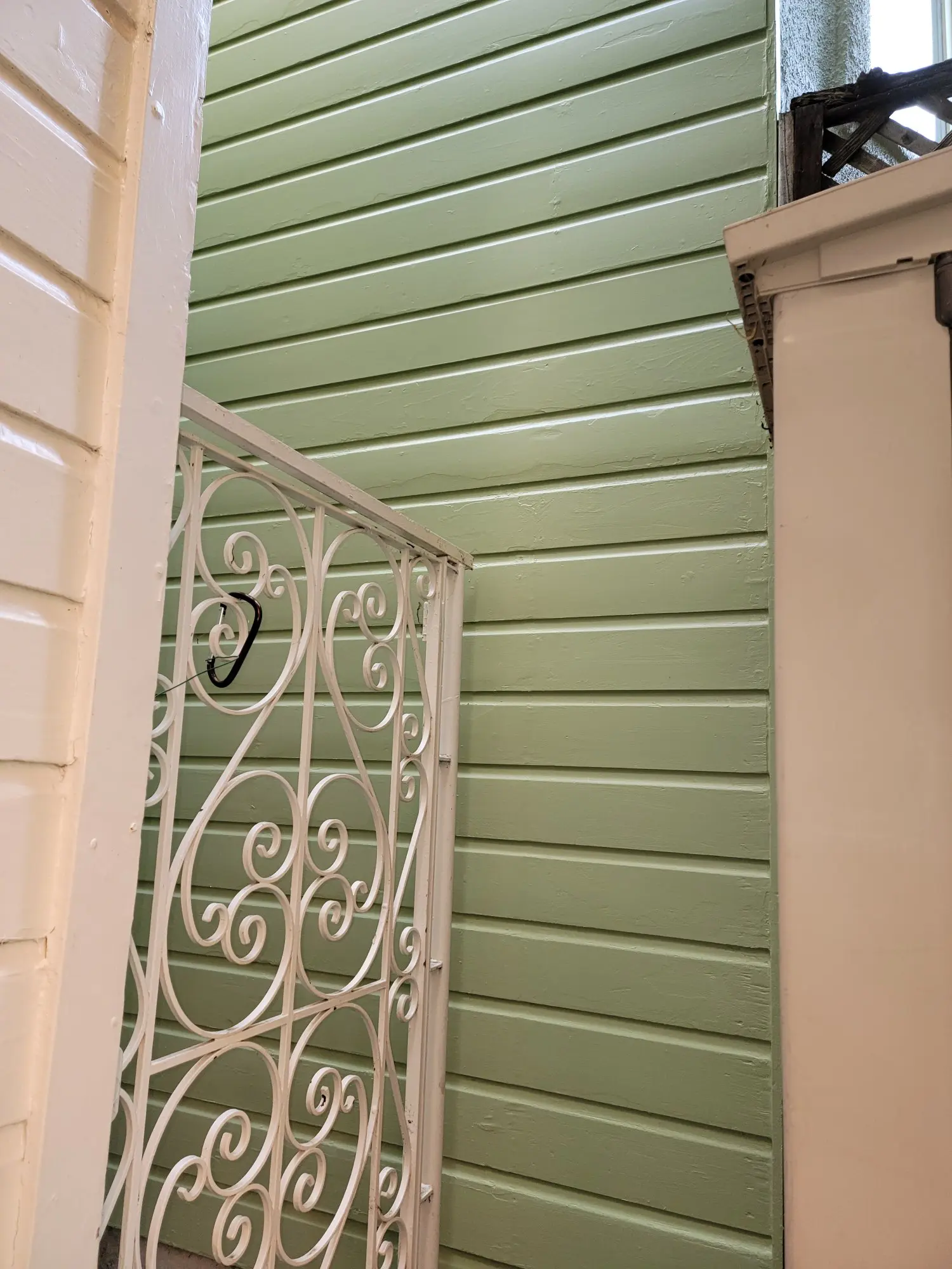 White ornate railing against green wooden wall.