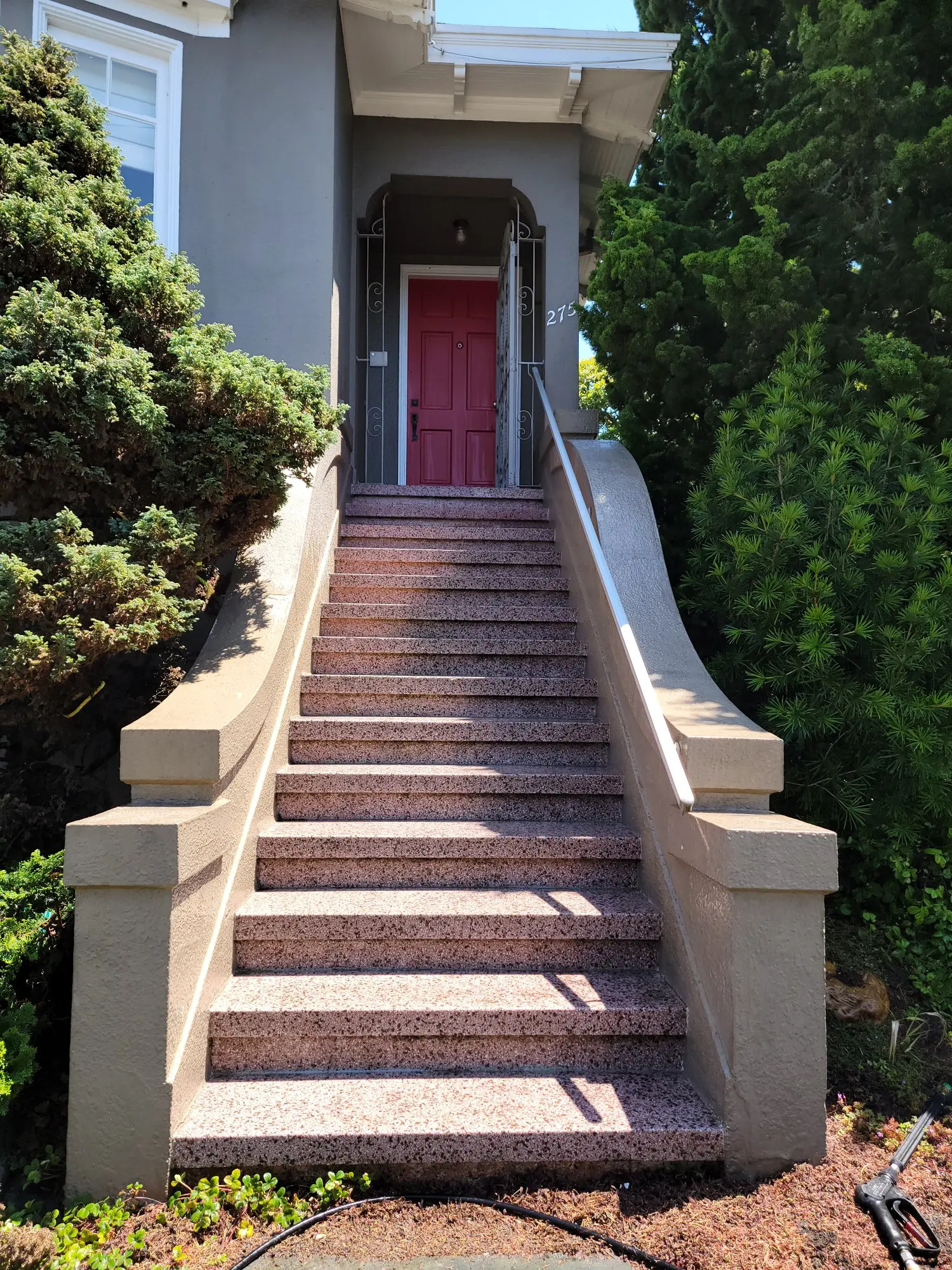 Stone staircase leading to a red door framed by greenery.