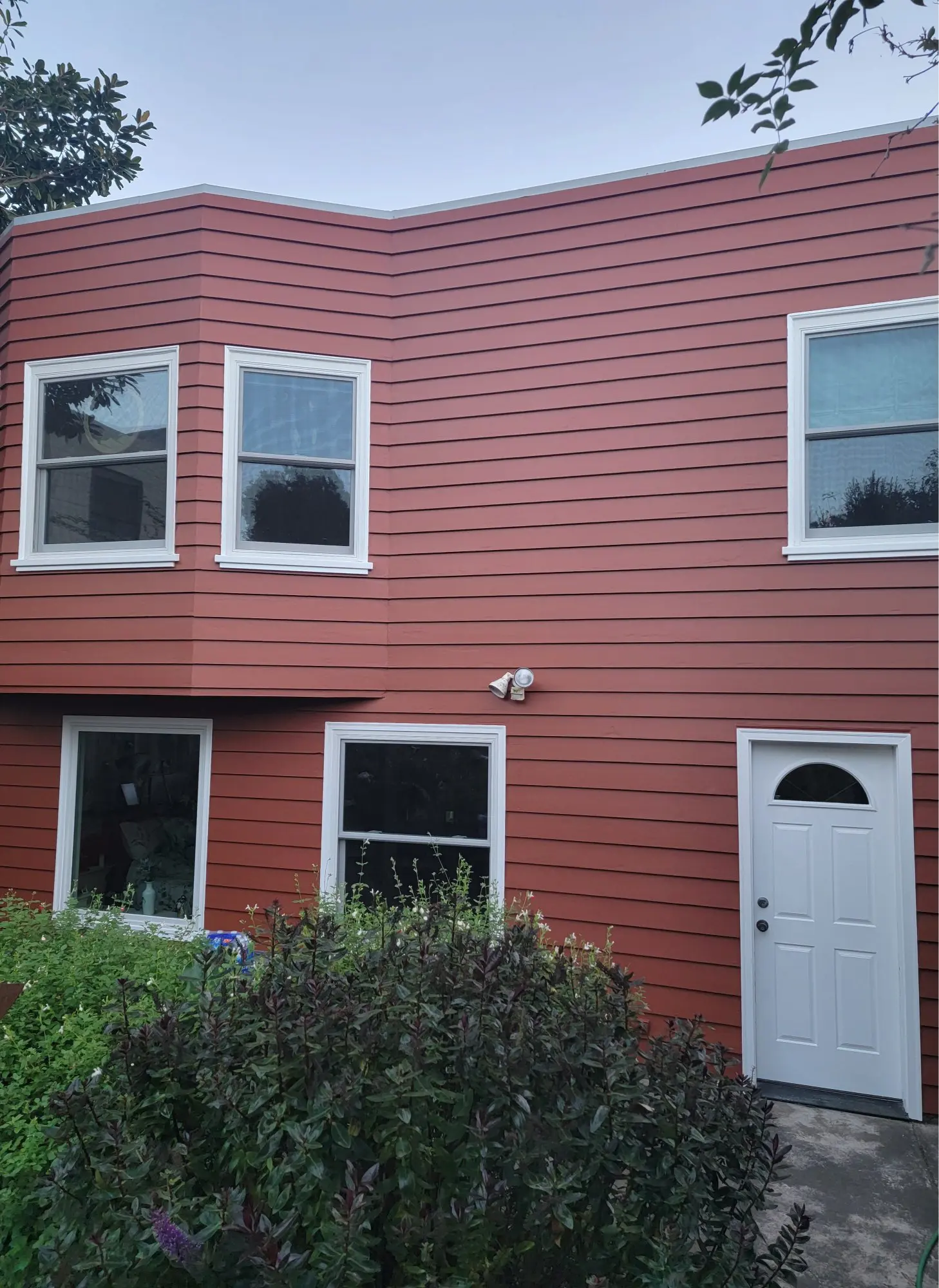 A red two-story house with white-trimmed windows and a white door.