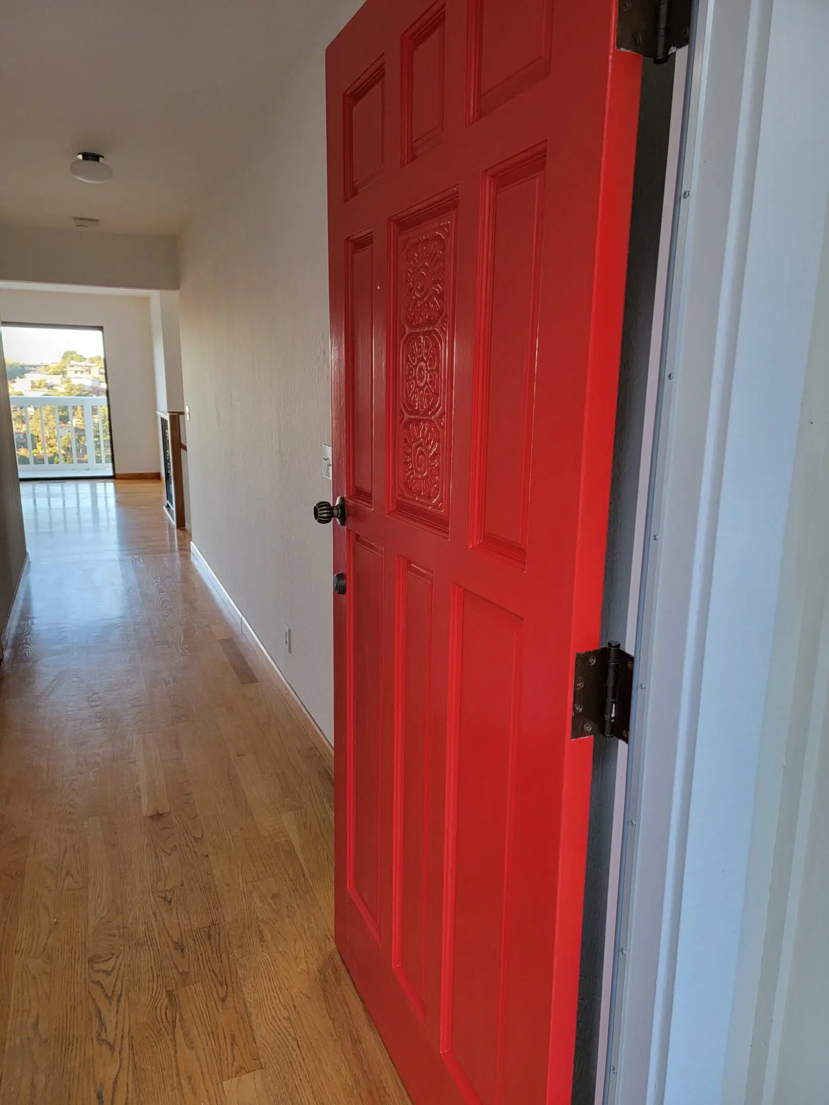 A bright red door stands open in a hallway with wooden floors.