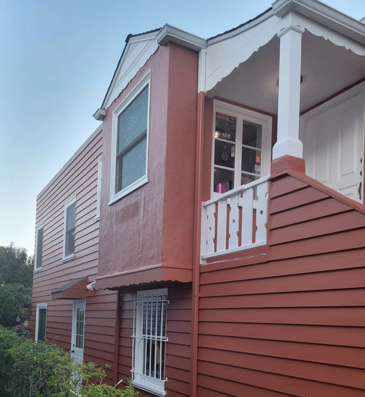Side view of a red two-story house with white trim and a small balcony.