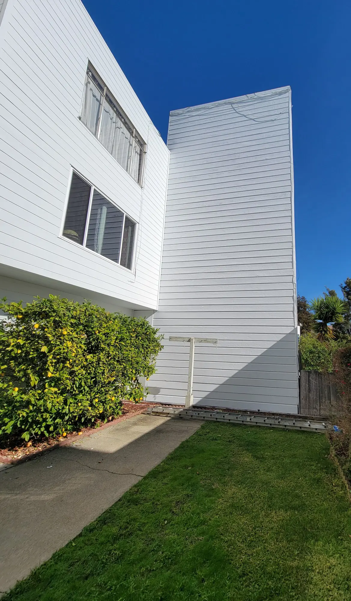 White brick building with green bushes and clear blue sky.