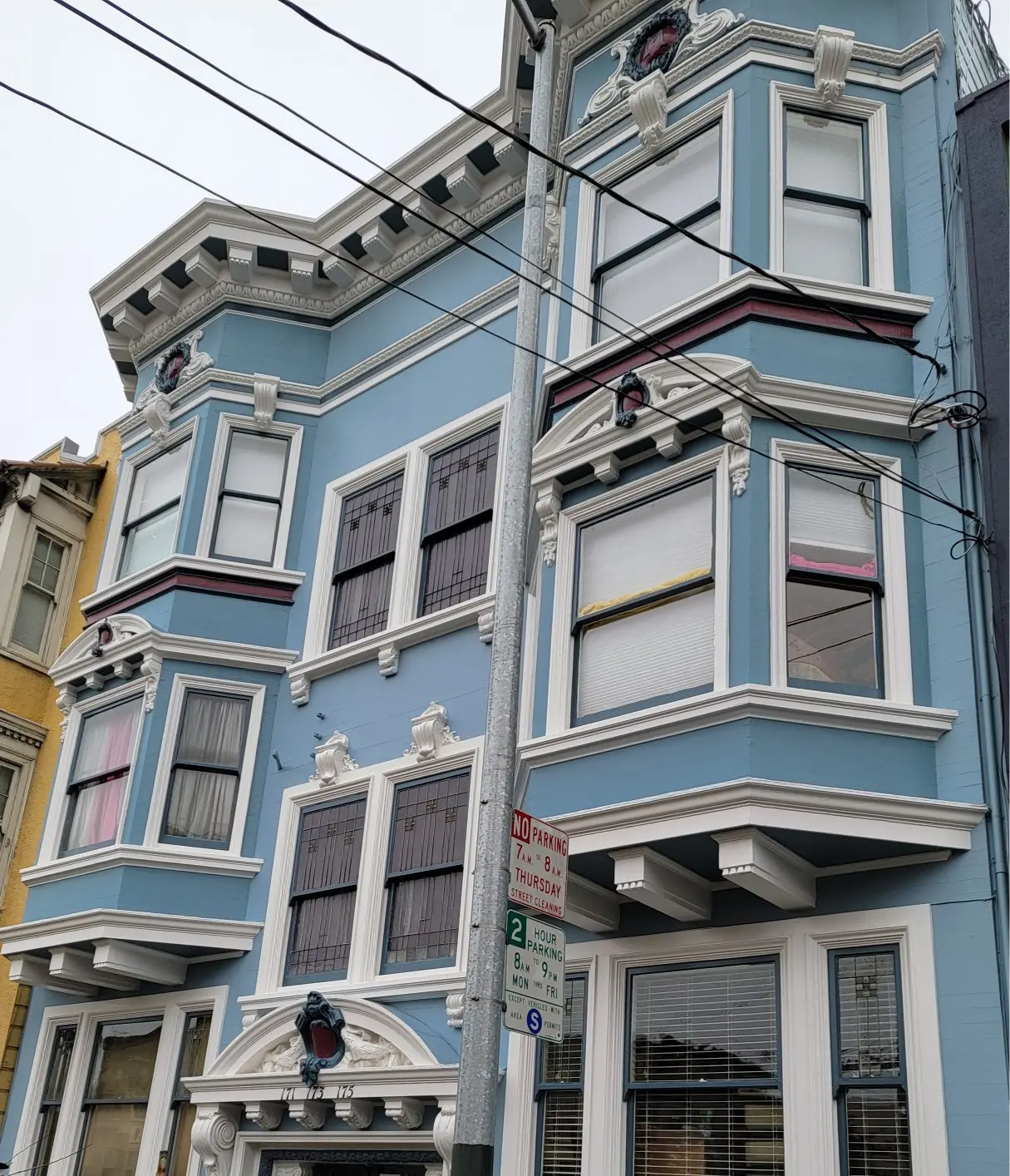 Blue Victorian-style house with bay windows on a city street.