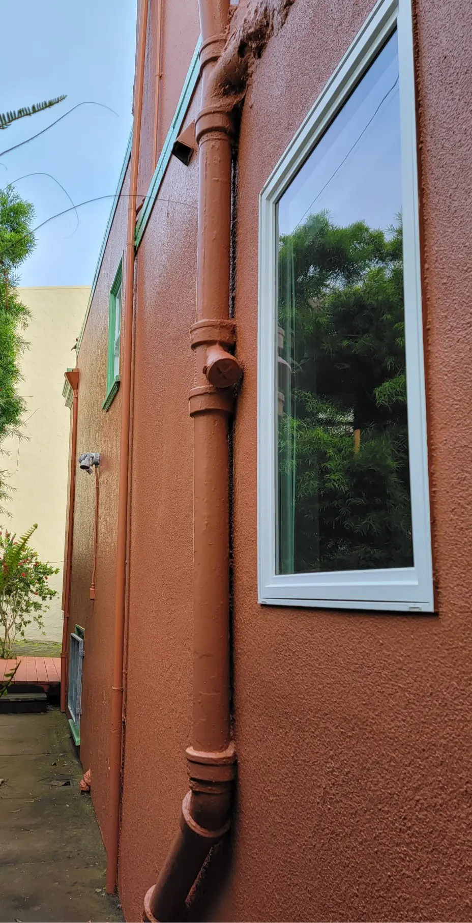 Close-up of a brown stucco house corner with a window and downspout.