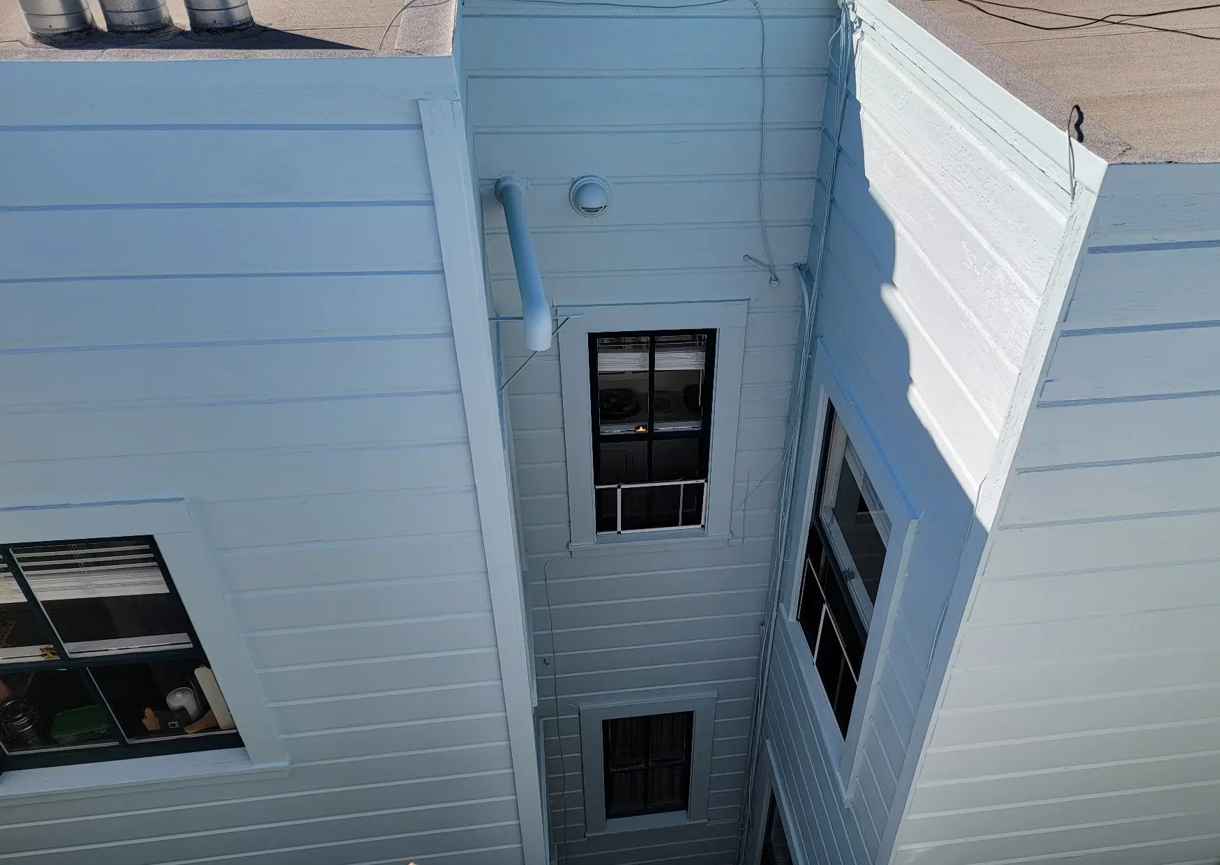 Looking up a narrow alley between white buildings with windows and an outdoor light.