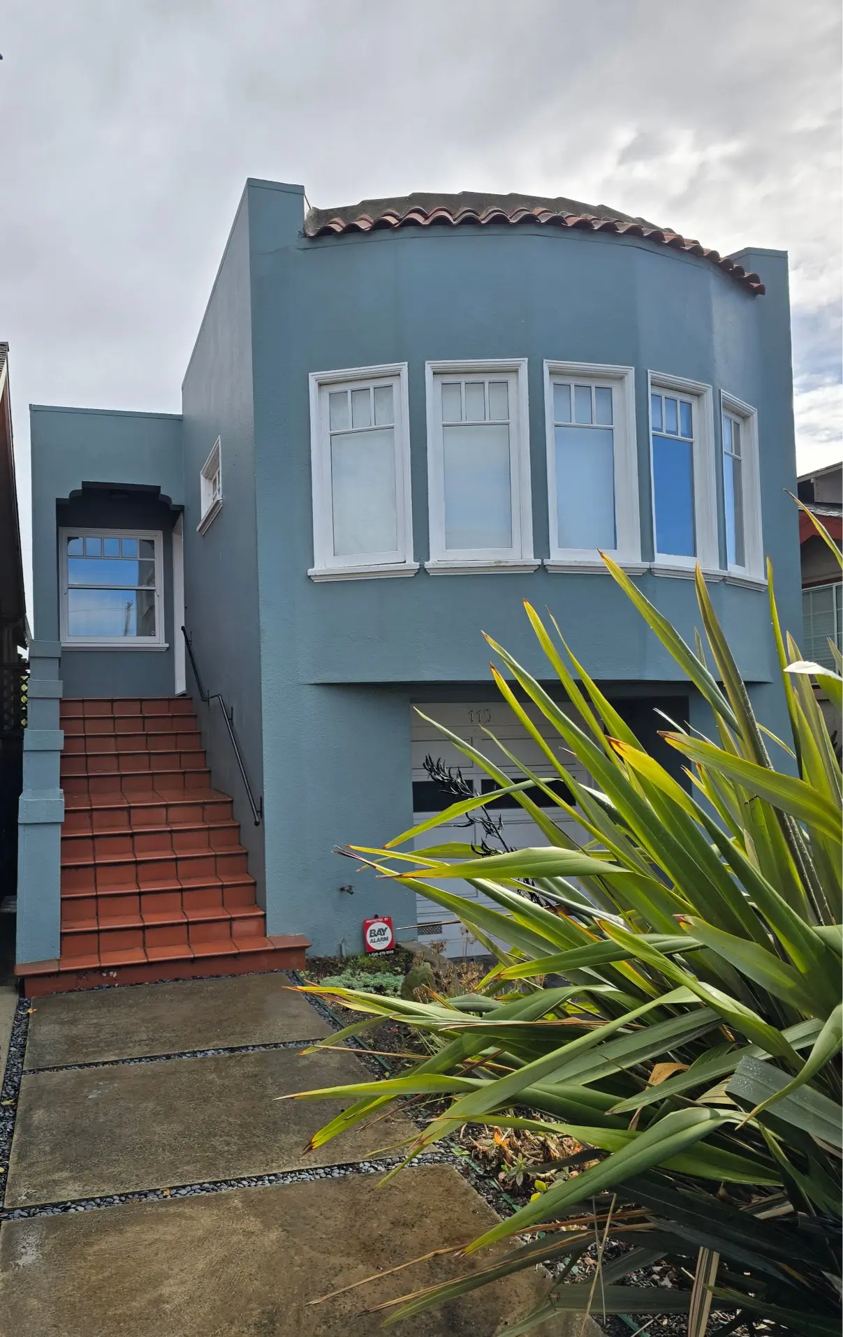 Blue house with stairs leading to a white door and multiple windows.