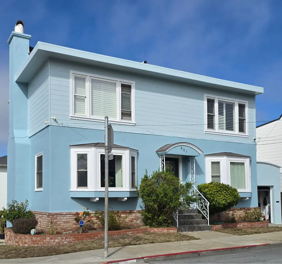 A two-story blue house with white trim on a sunny day.
