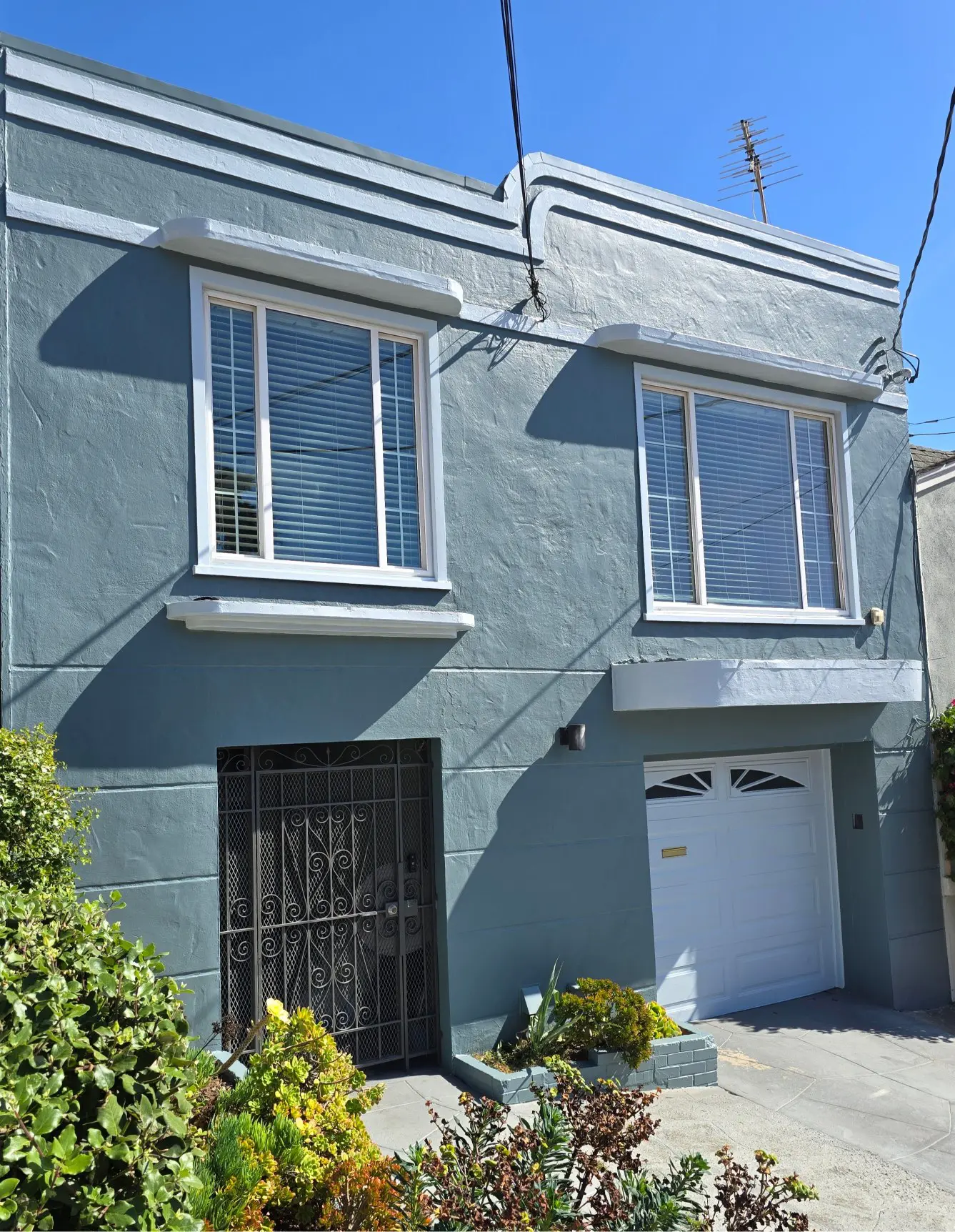 Gray two-story house with a garage and garden plants.