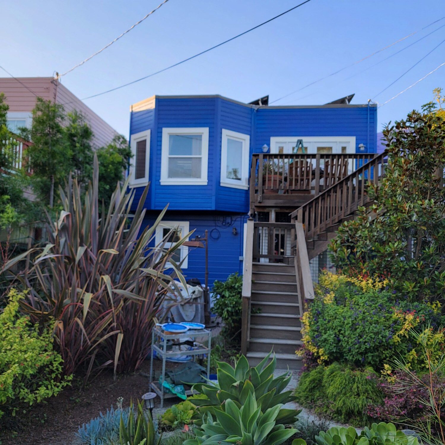 Blue house with a wooden staircase and lush garden.