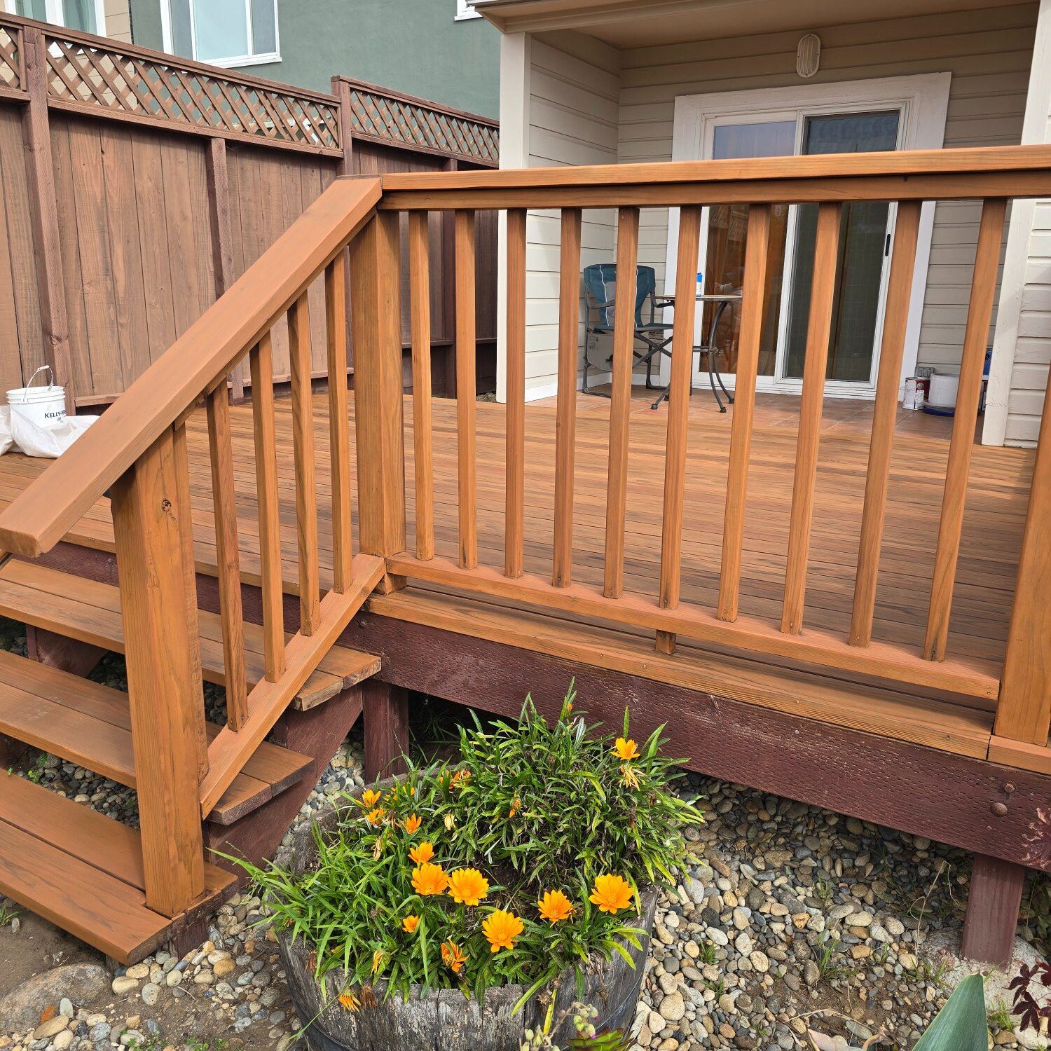 Wooden deck stairs leading to a patio with a flower bed below.